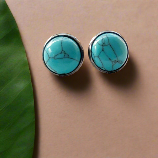 Round turquoise stud earrings with dark silver-tone setting displayed on a wood background