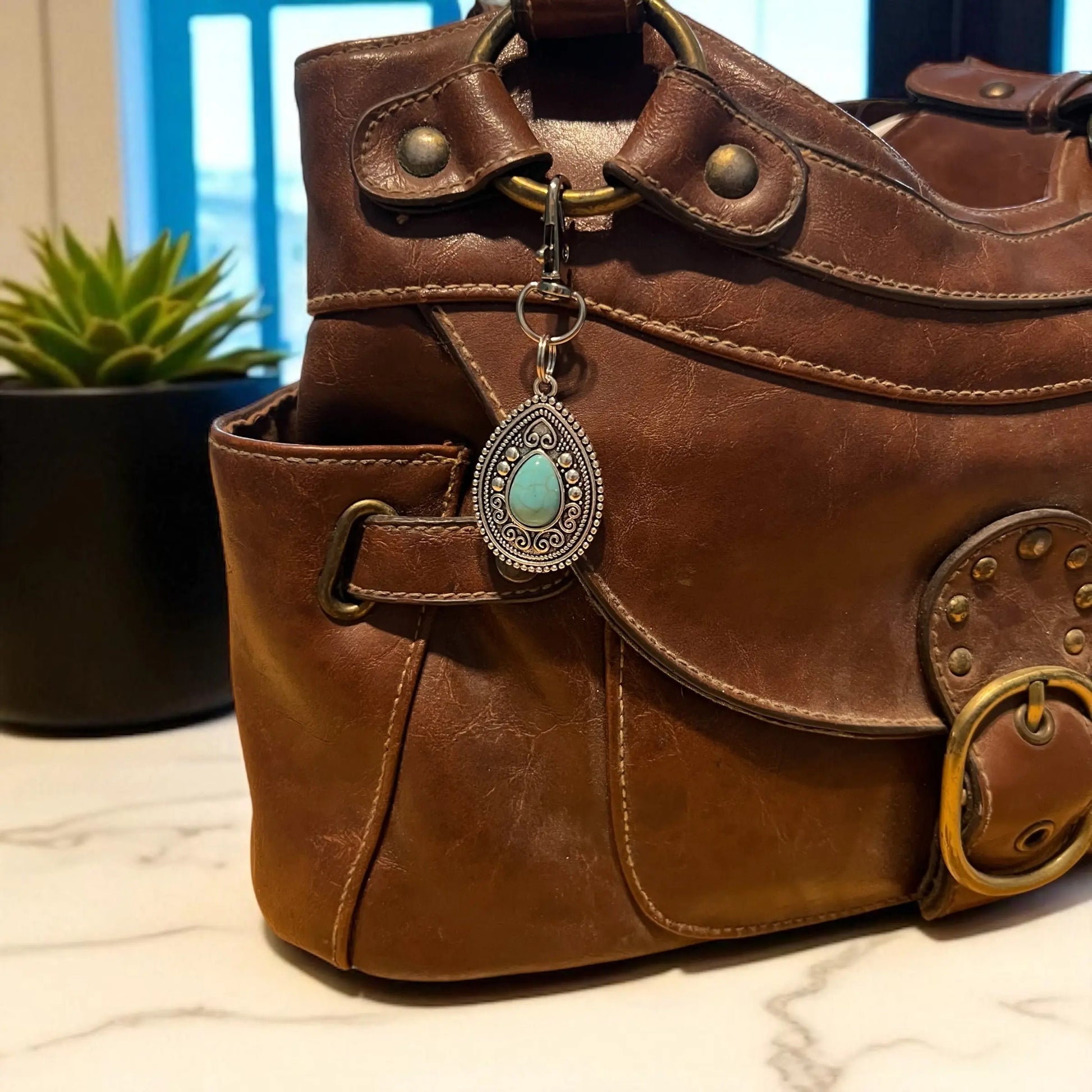 Silver western handbag charm with ornate medallion detail and faux turquoise accent clipped on a purse 