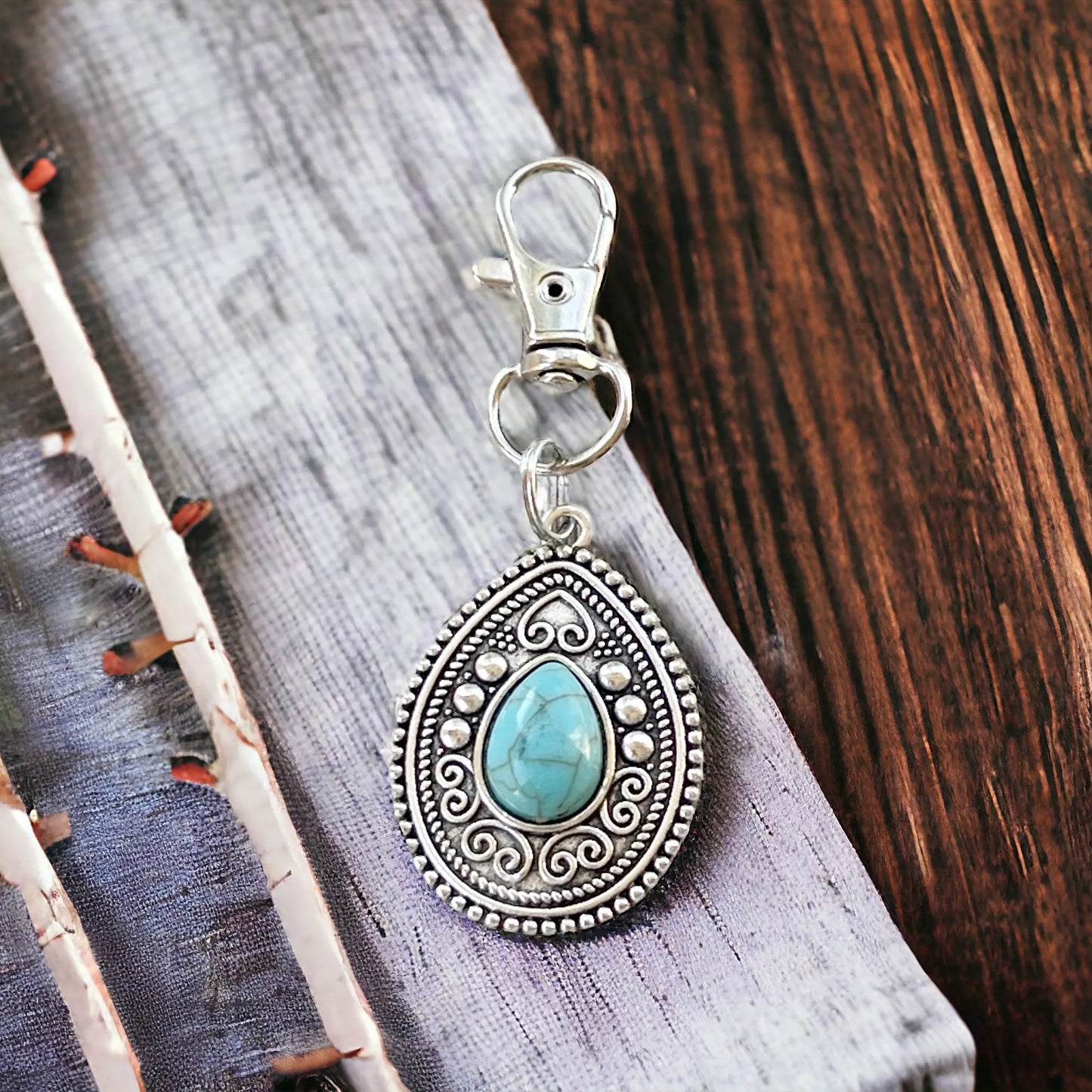 Silver western handbag charm with faux turquoise accent on a styled wooden display 