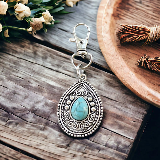 Silver western handbag charm with ornate medallion detail and faux turquoise accent on a styled display