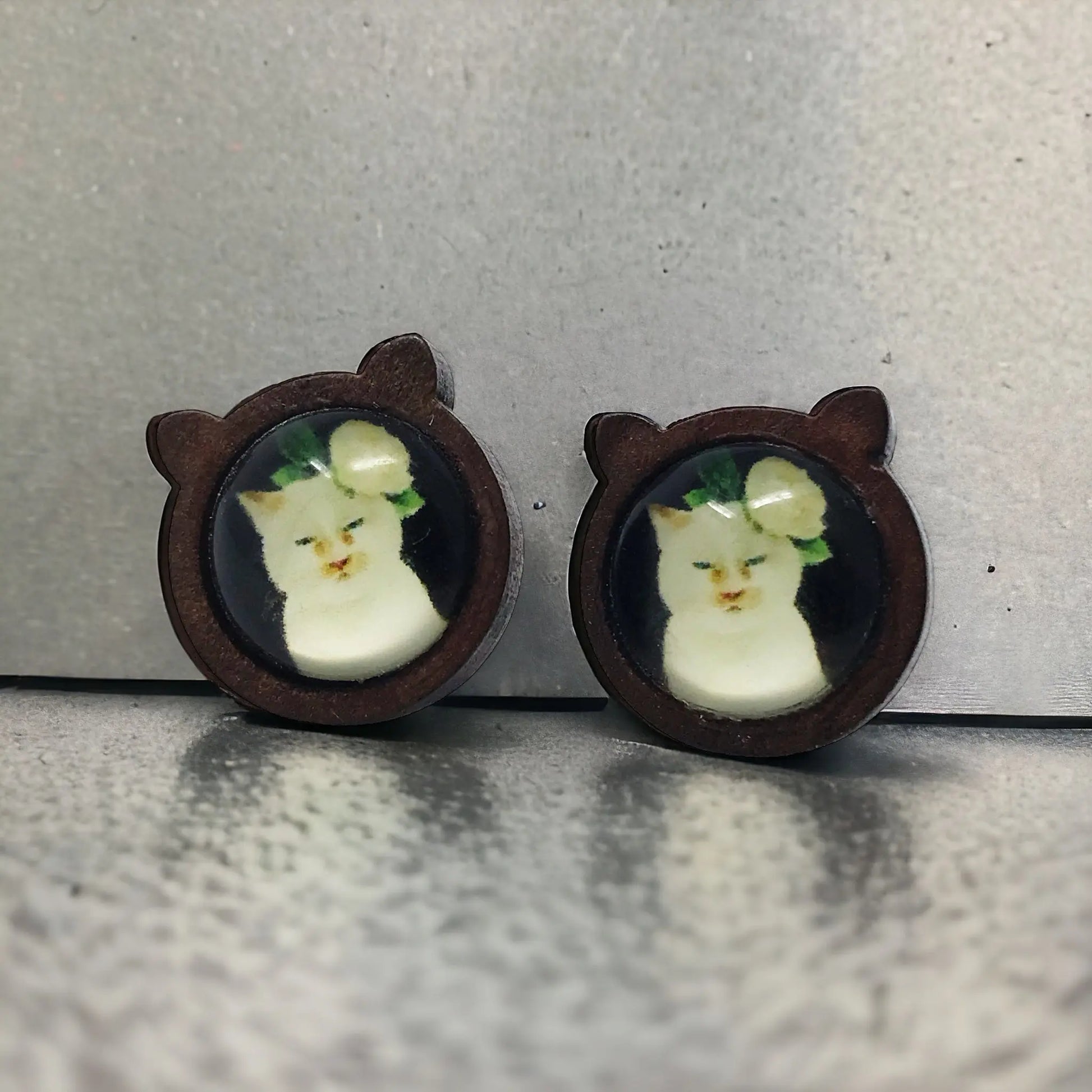 Pair of earrings with cat-shaped brown frames on a gray background