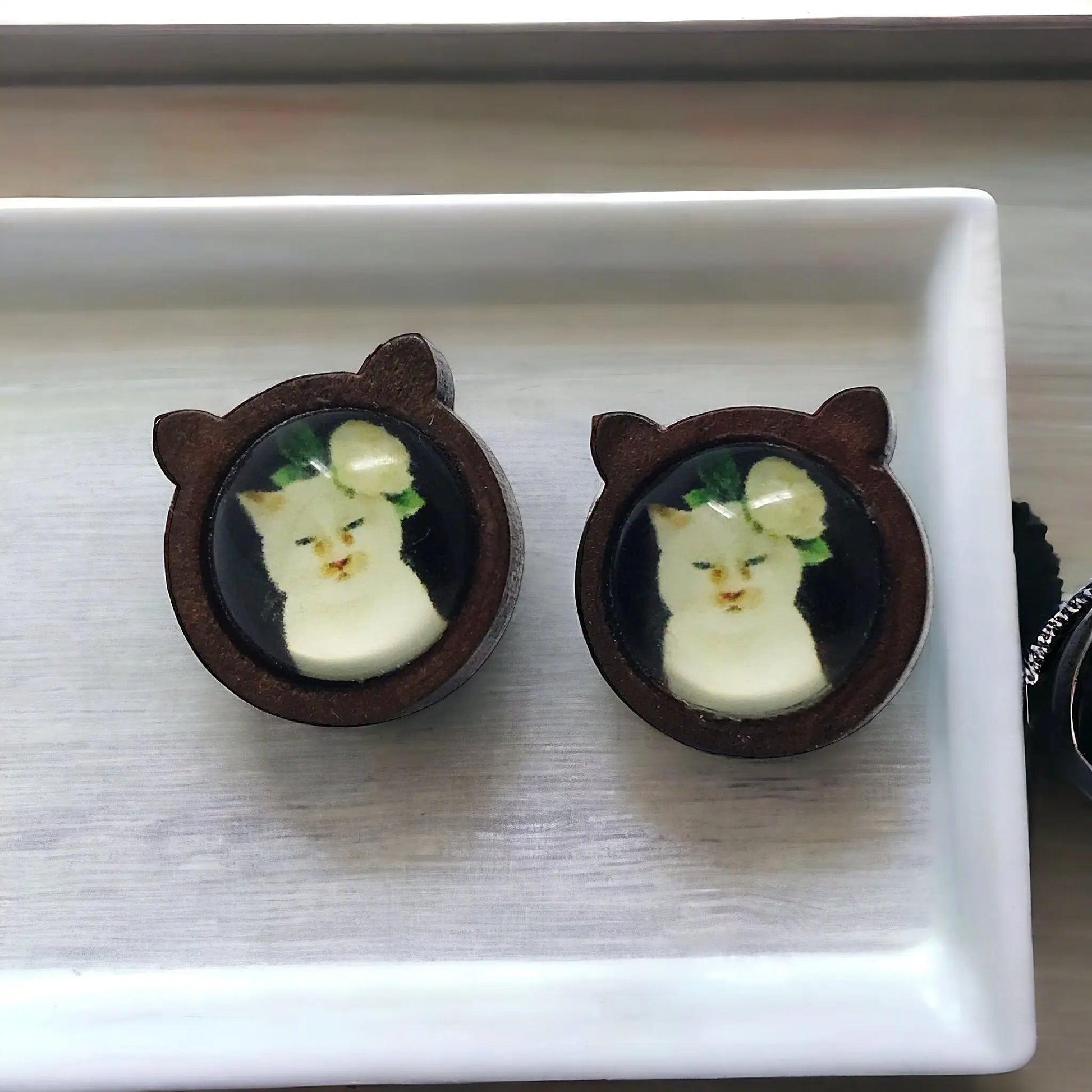 Pair of cat-shaped earrings with a floral cat design on a white tray.