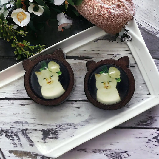 Two cat-shaped earrings with embedded images on a white tray.