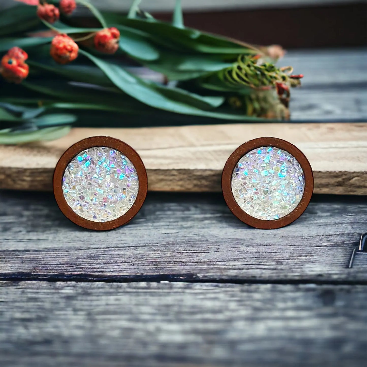 Round white glitter druzy wood stud earrings displayed on a rustic wood surface With flowers 