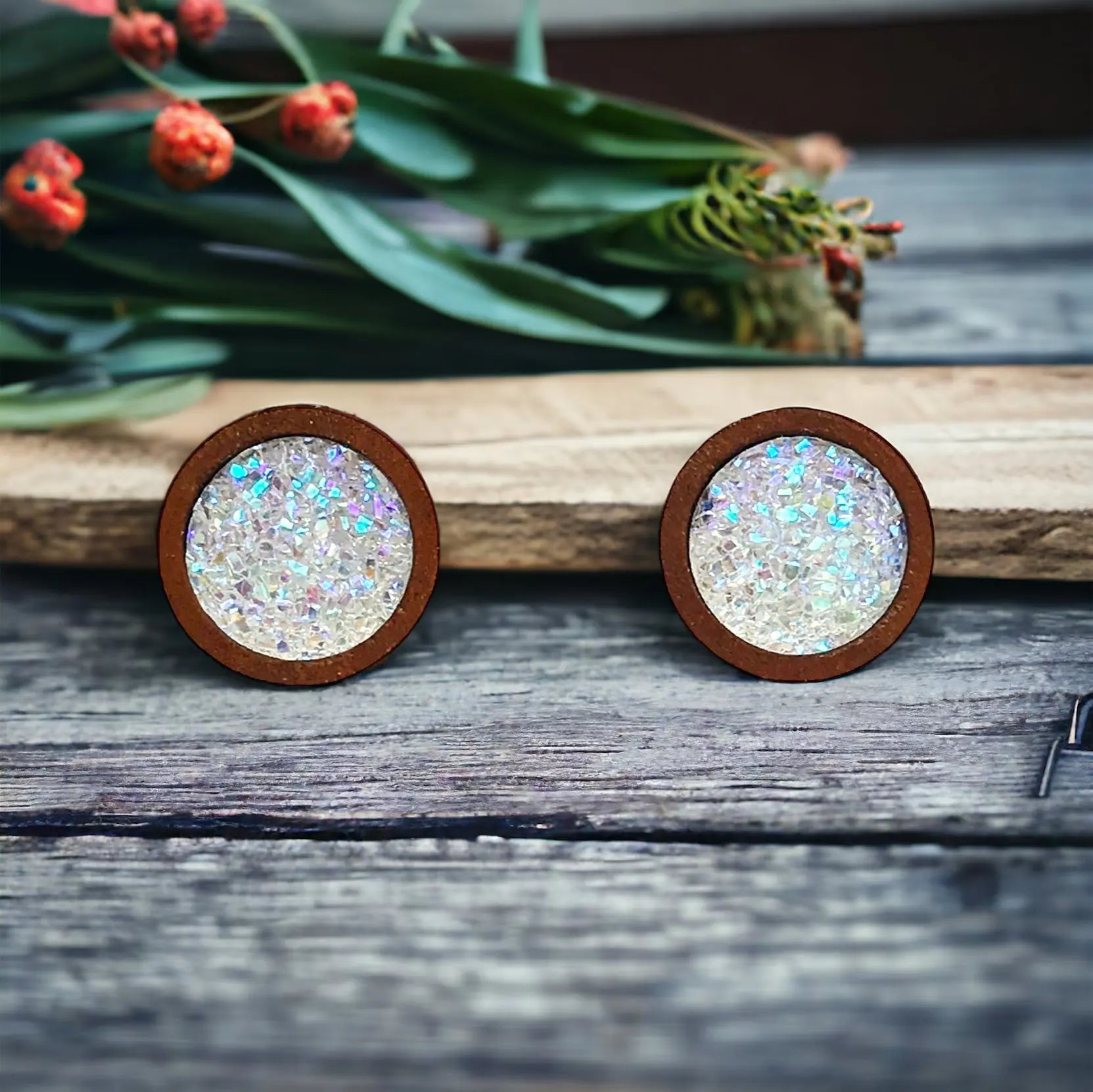 Round white glitter druzy wood stud earrings displayed on a rustic wood surface With flowers 