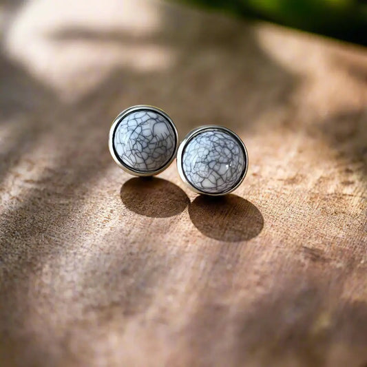 Round white stone stud earrings with silver-tone setting displayed on a wood background
