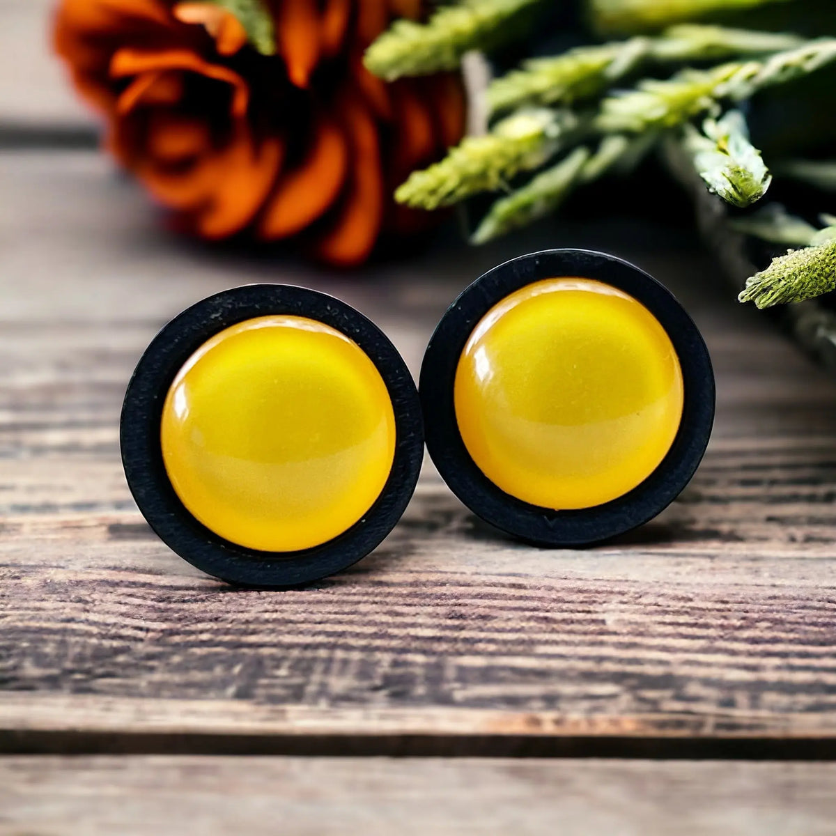 Yellow round earrings with black borders on a boho wooden surface.