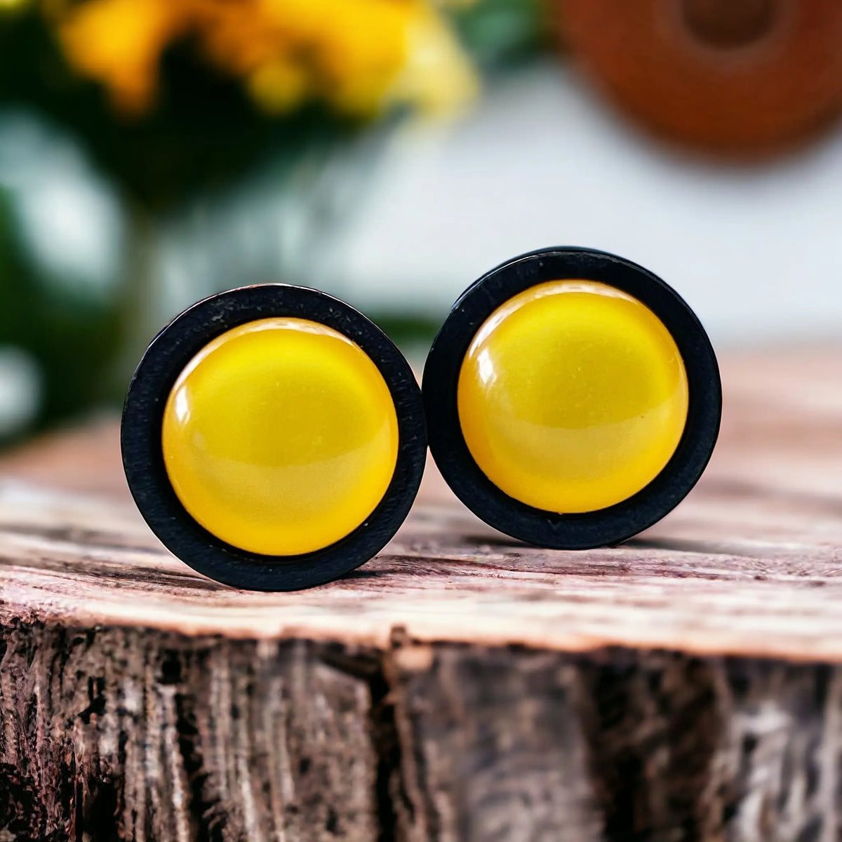 Pair of yellow round earrings with black wood rims on a wooden surface.