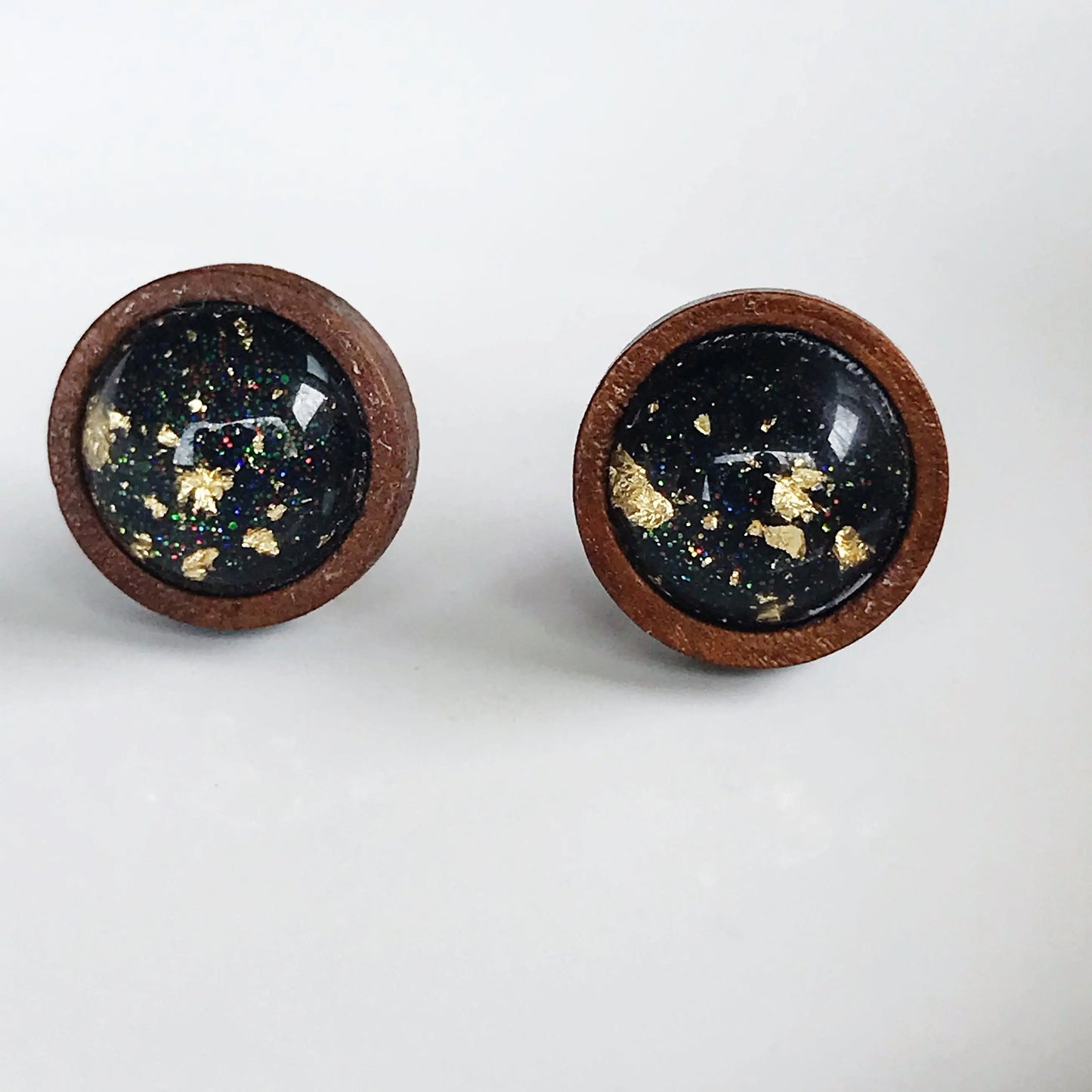 Back of round black resin wood stud earrings with gold flake detail and subtle sparkle on a neutral background 