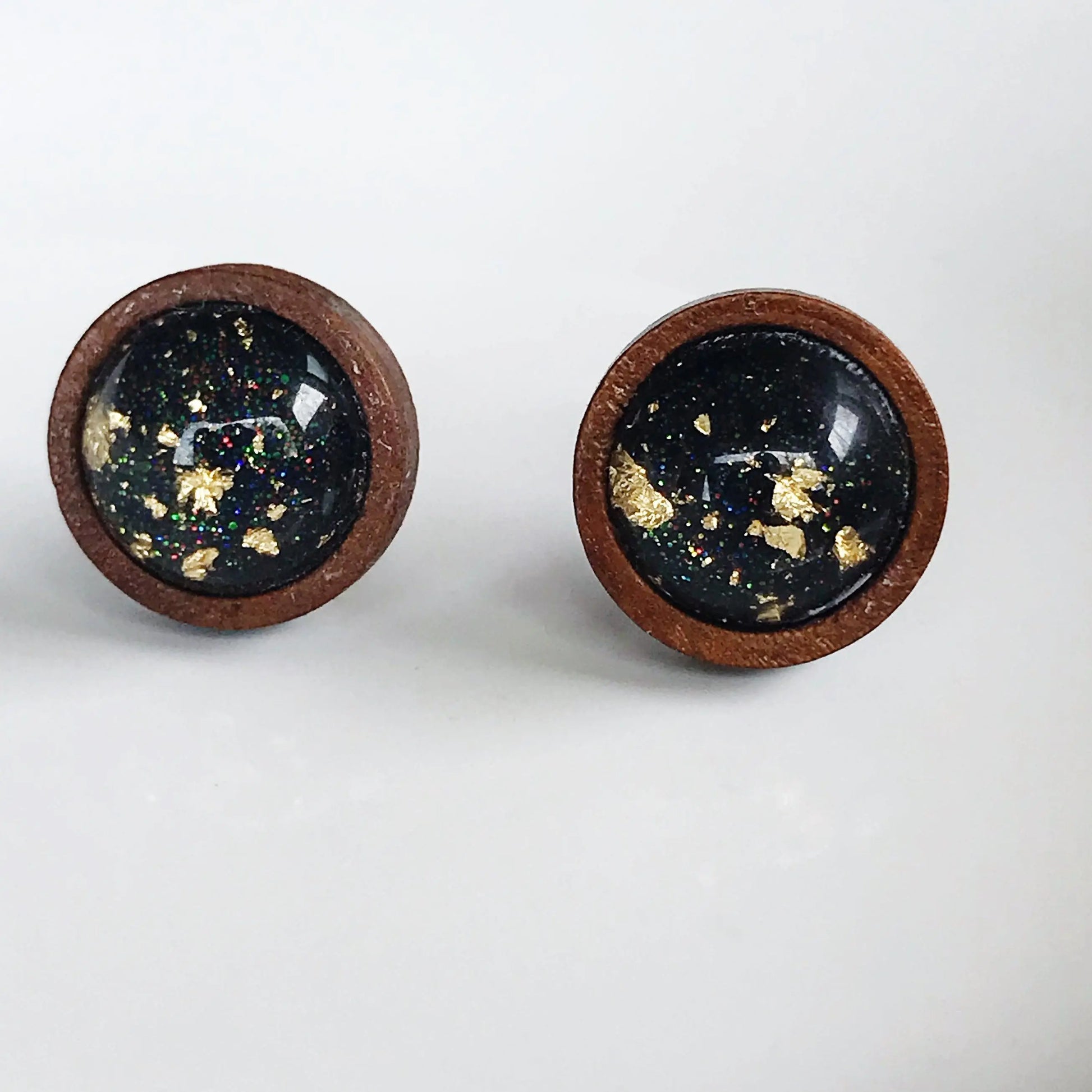 Back of round black resin wood stud earrings with gold flake detail and subtle sparkle on a neutral background 