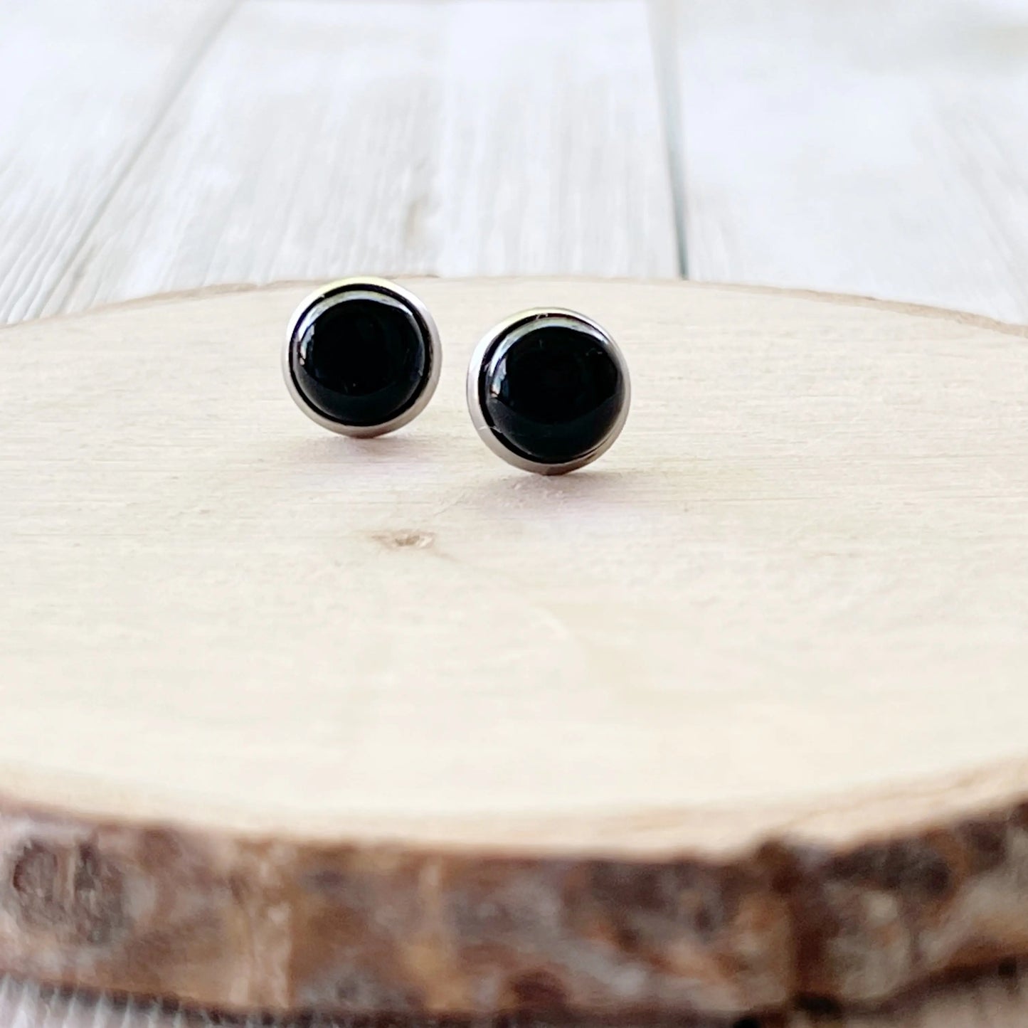 Round black onyx-style stud earrings in a silver-tone setting displayed on a light wood slice background