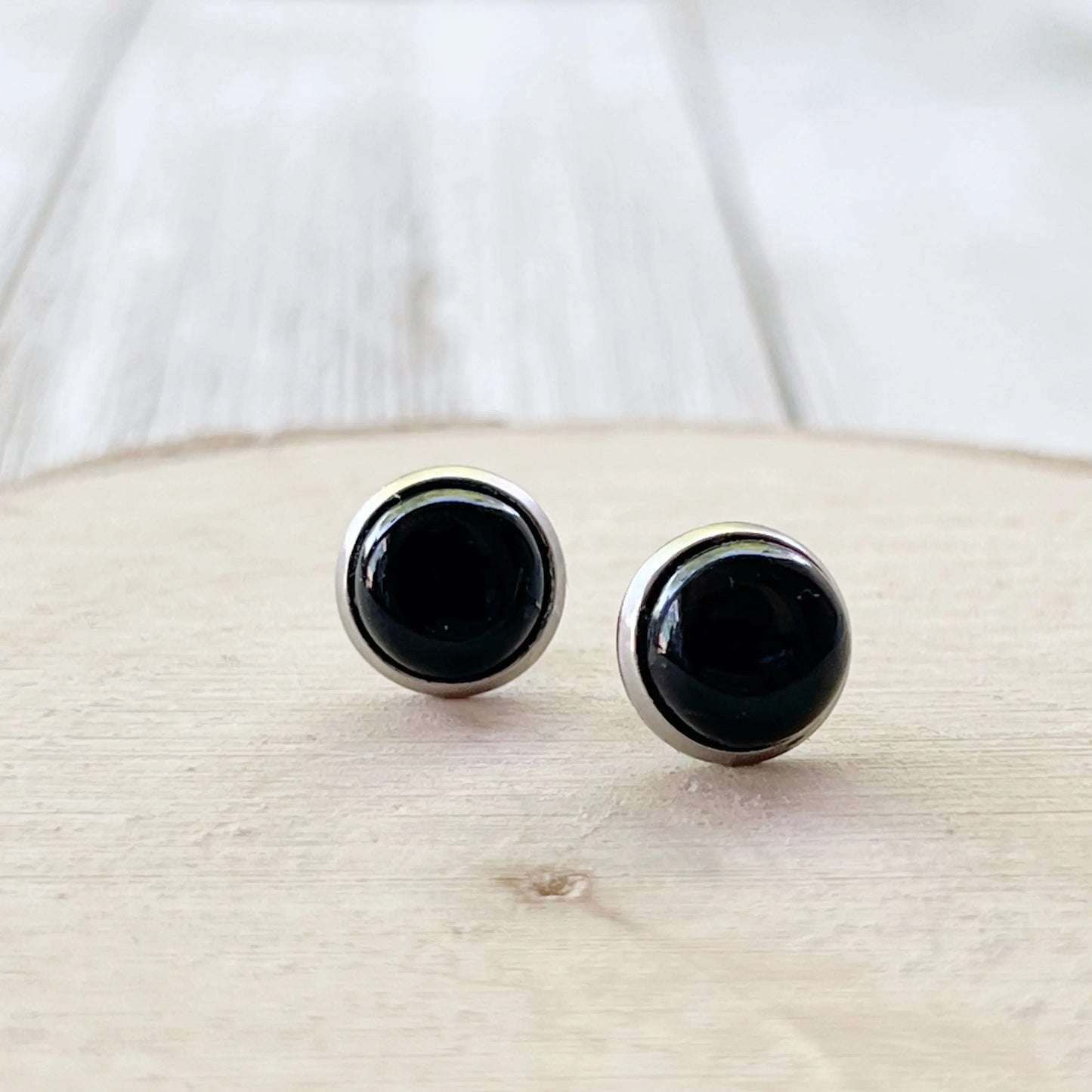 Side view of round black onyx-style stud earrings in a silver-tone setting displayed on a light wood background