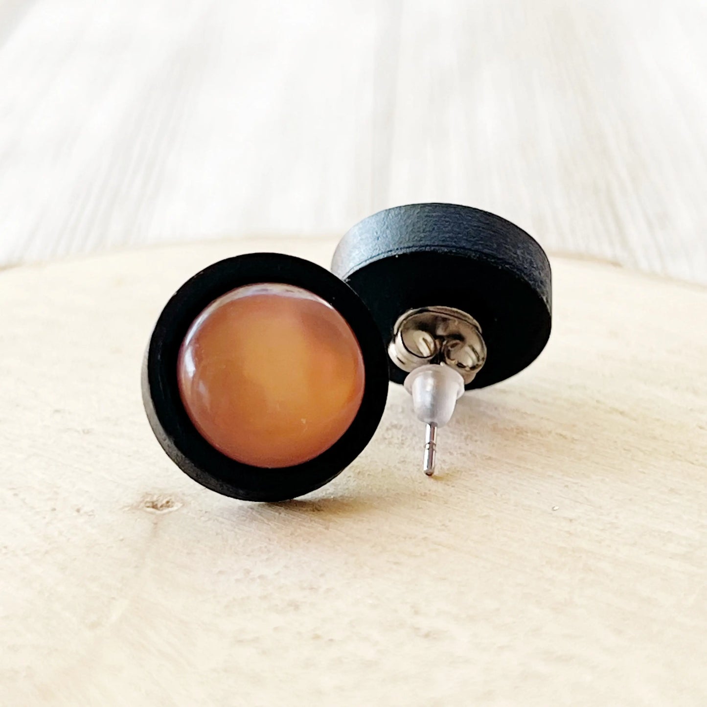 Black earrings with brown round stones on a light wooden surface displaying back of earrings