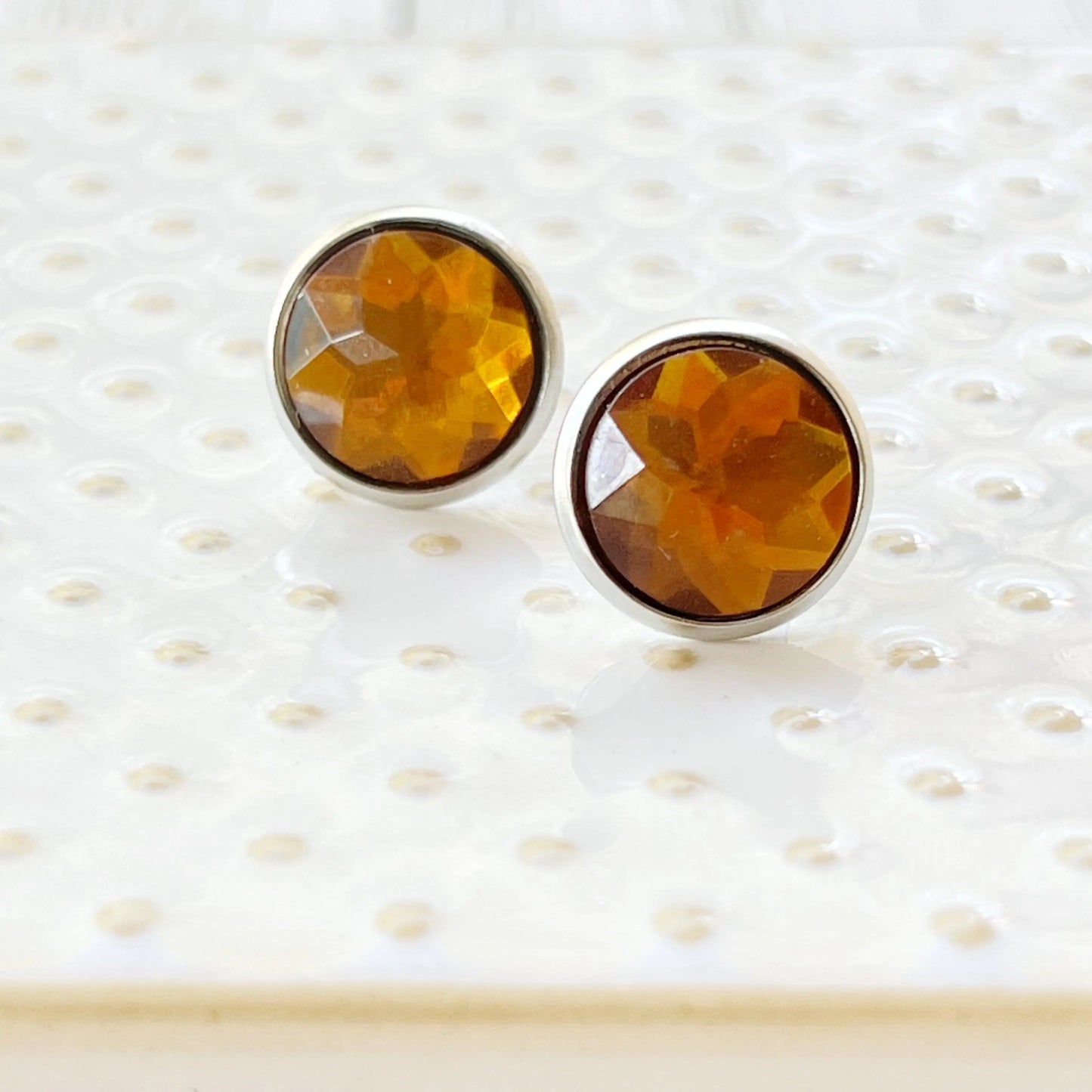 Round citrine honey brown faceted stud earrings in a silver-tone setting displayed on a white dish