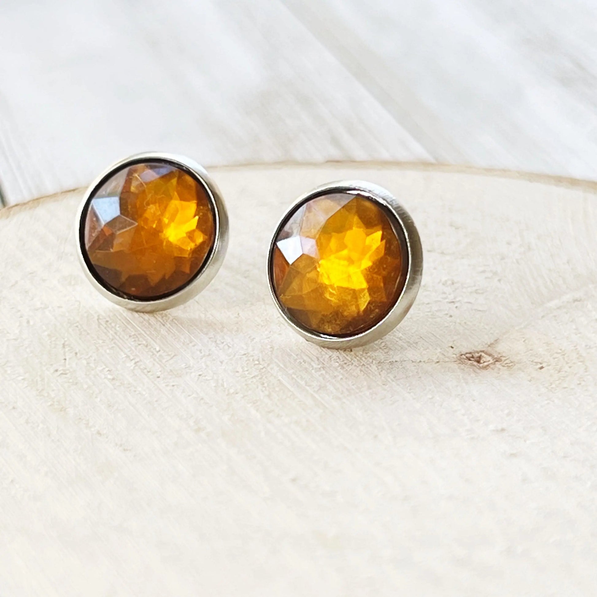 Pair of amber-colored stud earrings on a light wooden surface