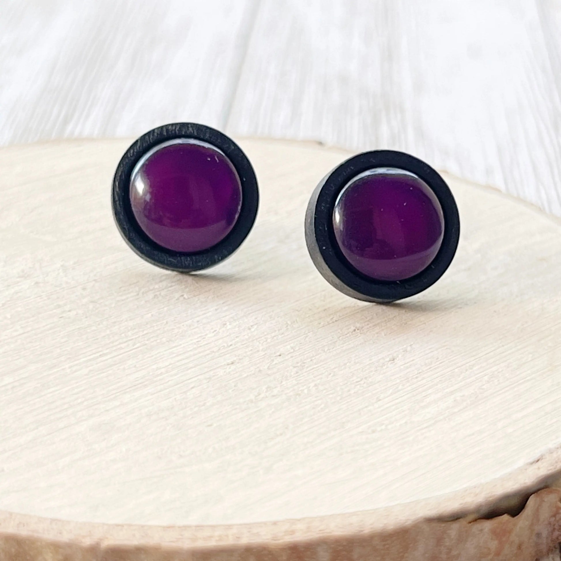 Purple round earrings with black wood rims on a whitewashed wood surface