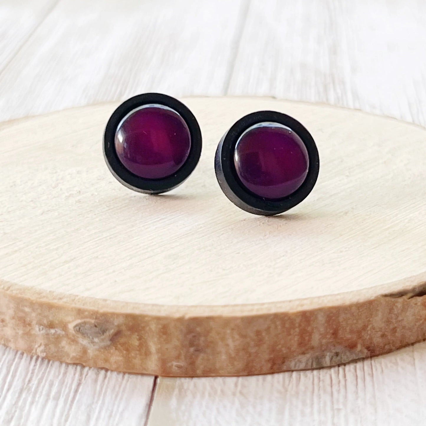 Pair of round earrings with purple centers on a wooden surface