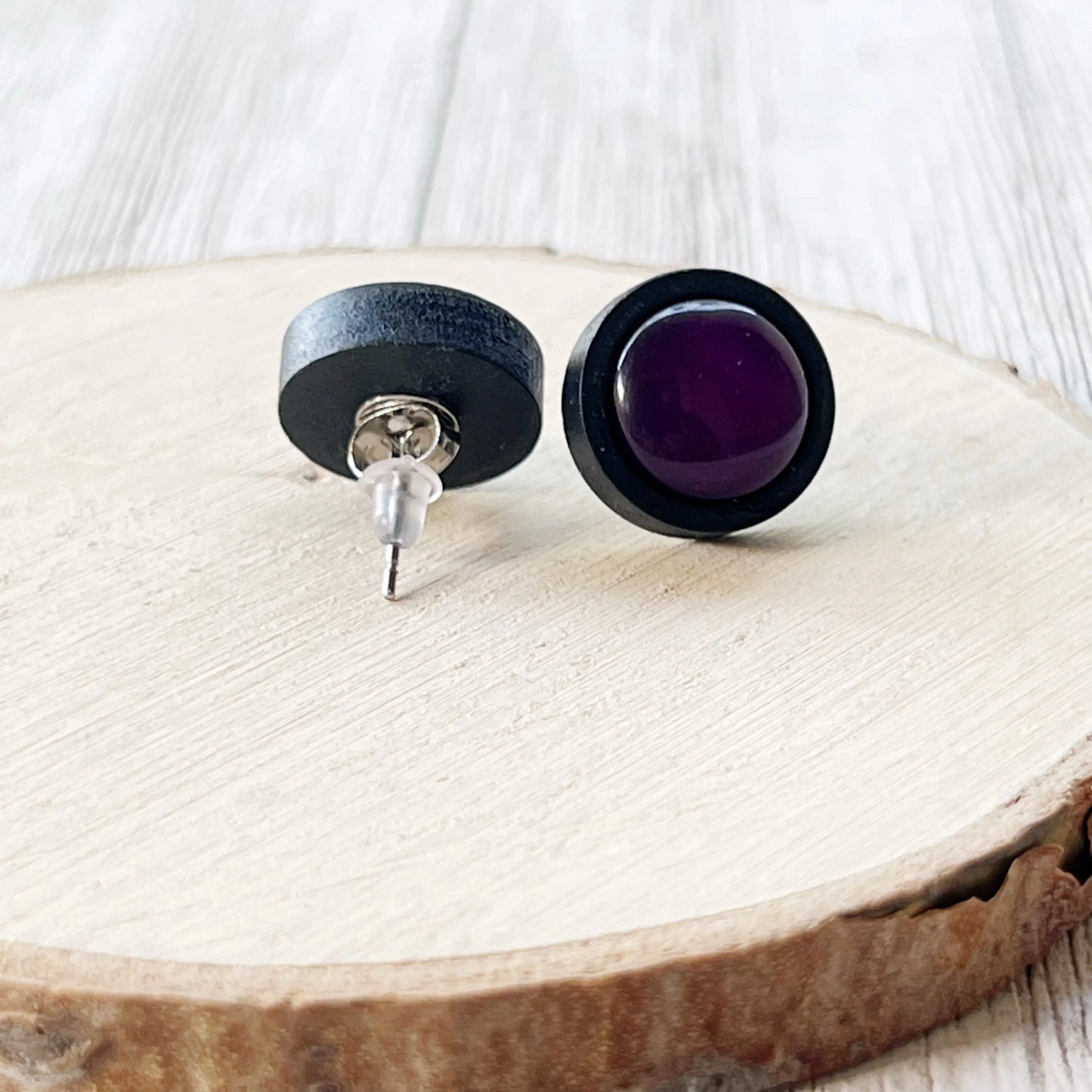 Back side of a pair of black and purple round earrings on a wooden surface