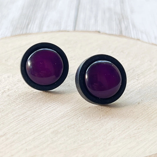 Round dark purple resin stud earrings with black wood borders displayed on a light wood surface