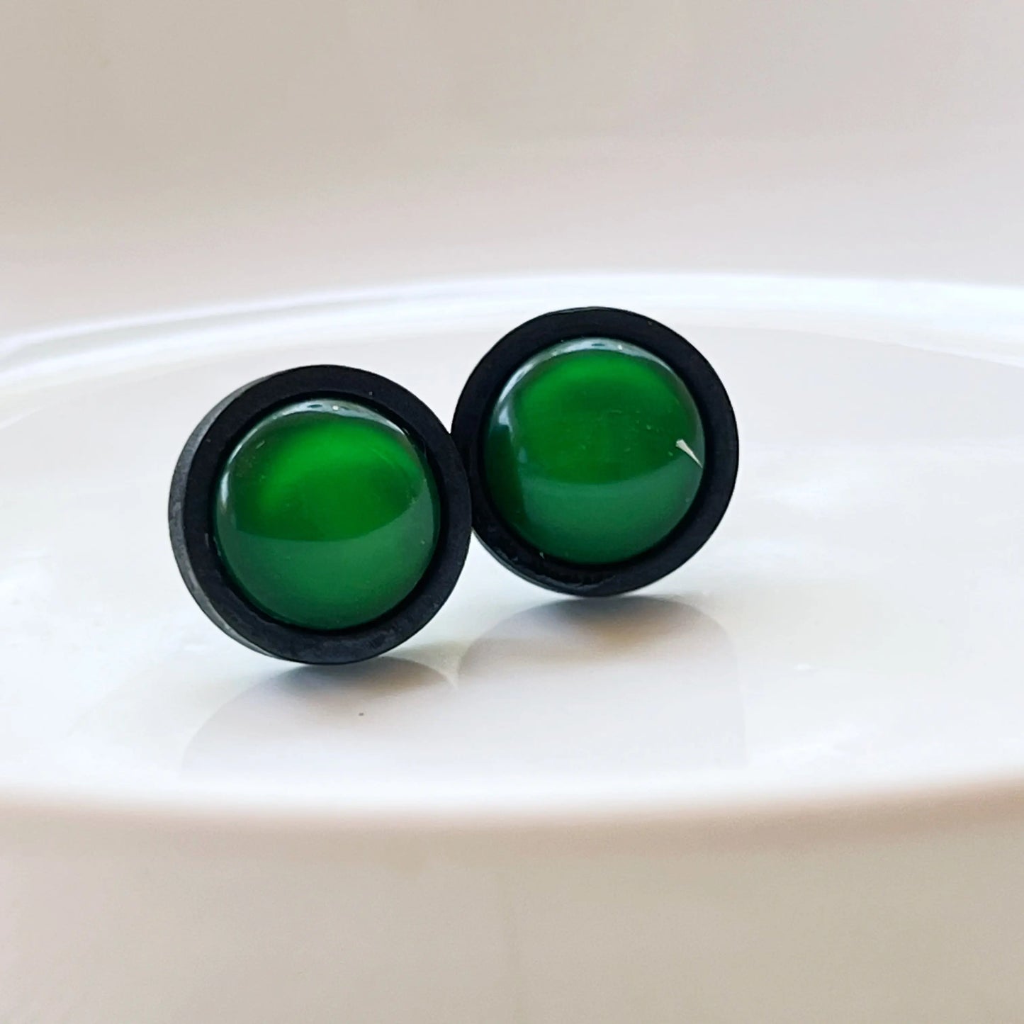 Green circular earrings with black borders on a white glass background