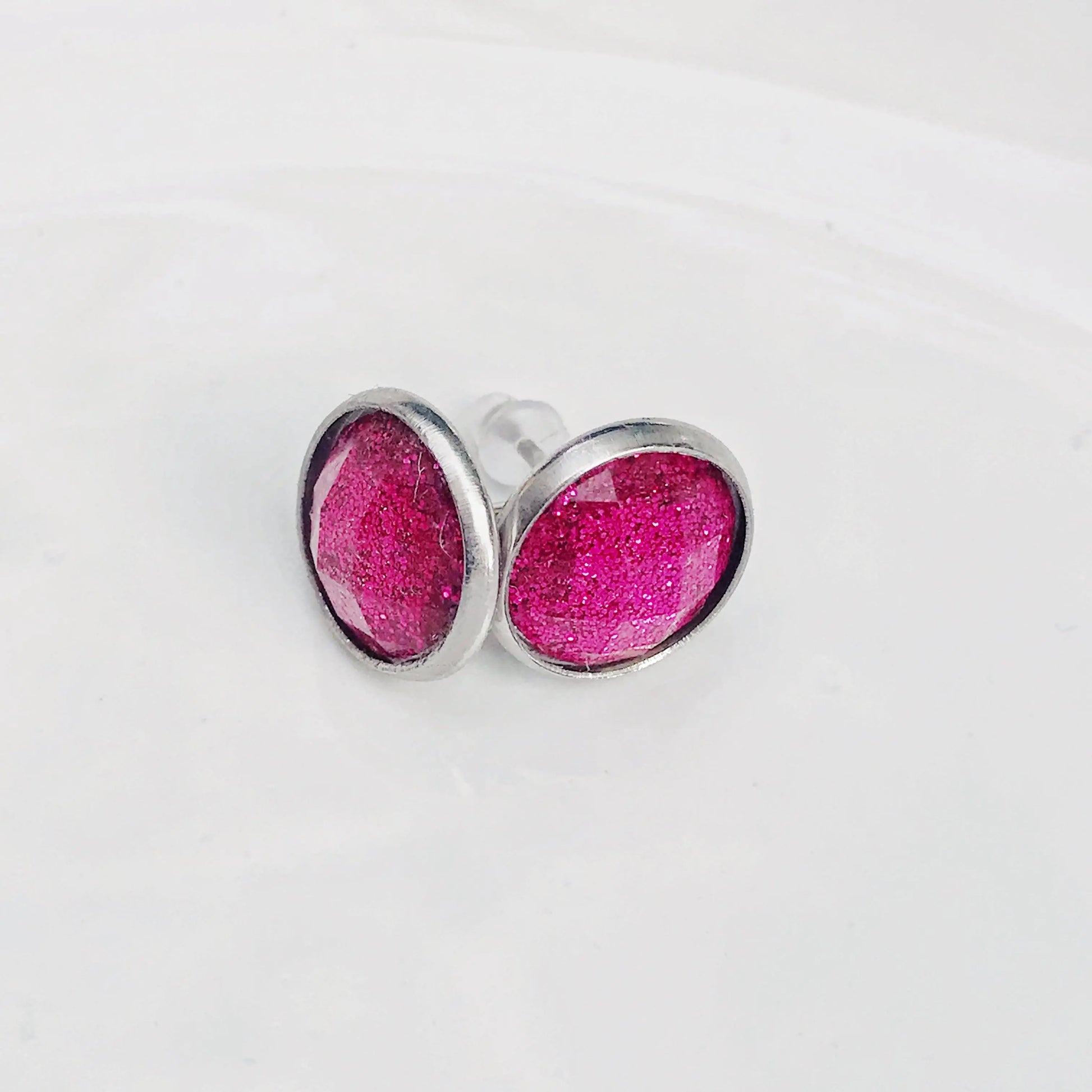 Round hot pink glitter stud earrings in a silver-tone setting displayed on a white background 