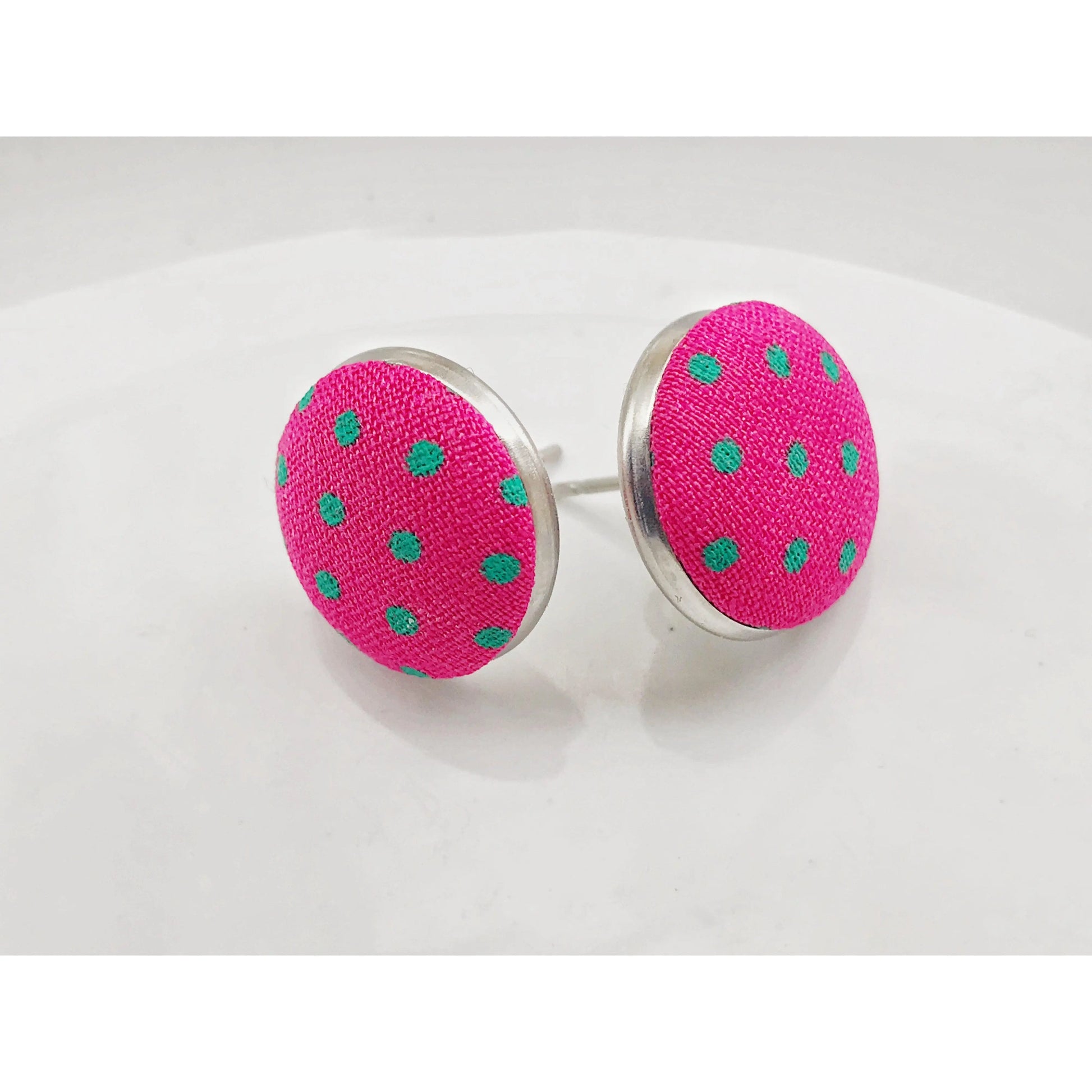 Round hot pink fabric stud earrings with mint green polka dots in a silver-tone setting displayed on a white surface