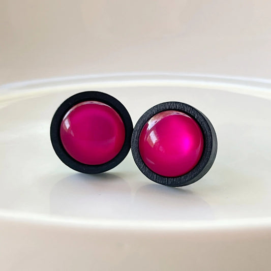 Round hot pink resin stud earrings with black wood border displayed on a white dish