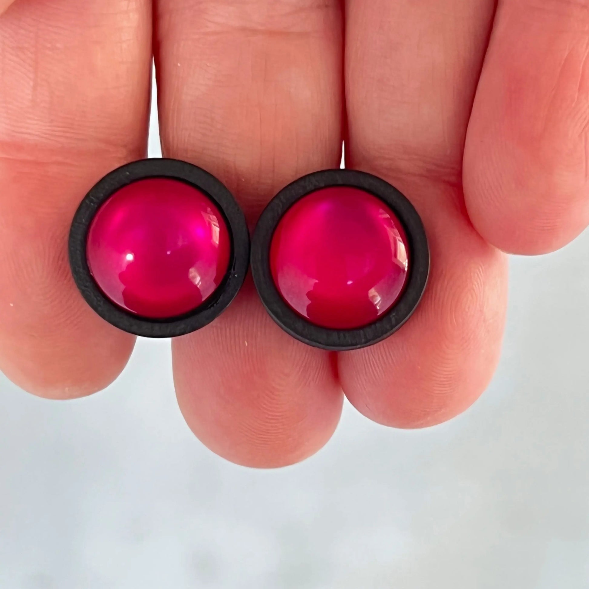 Pink earrings with black rims held between fingers against a white background