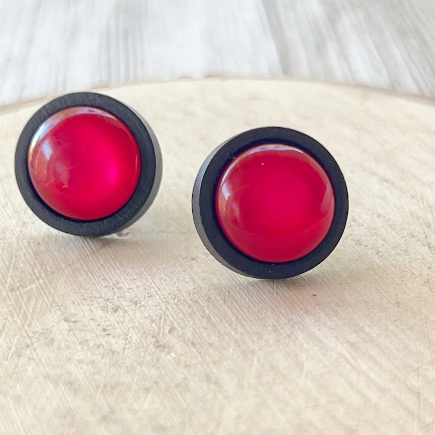 Pair of pink round earrings with black rims on a light wooden surface.