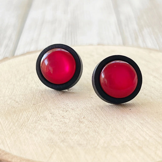 Pair of round earrings with Pink centers and black rims on a wooden surface.