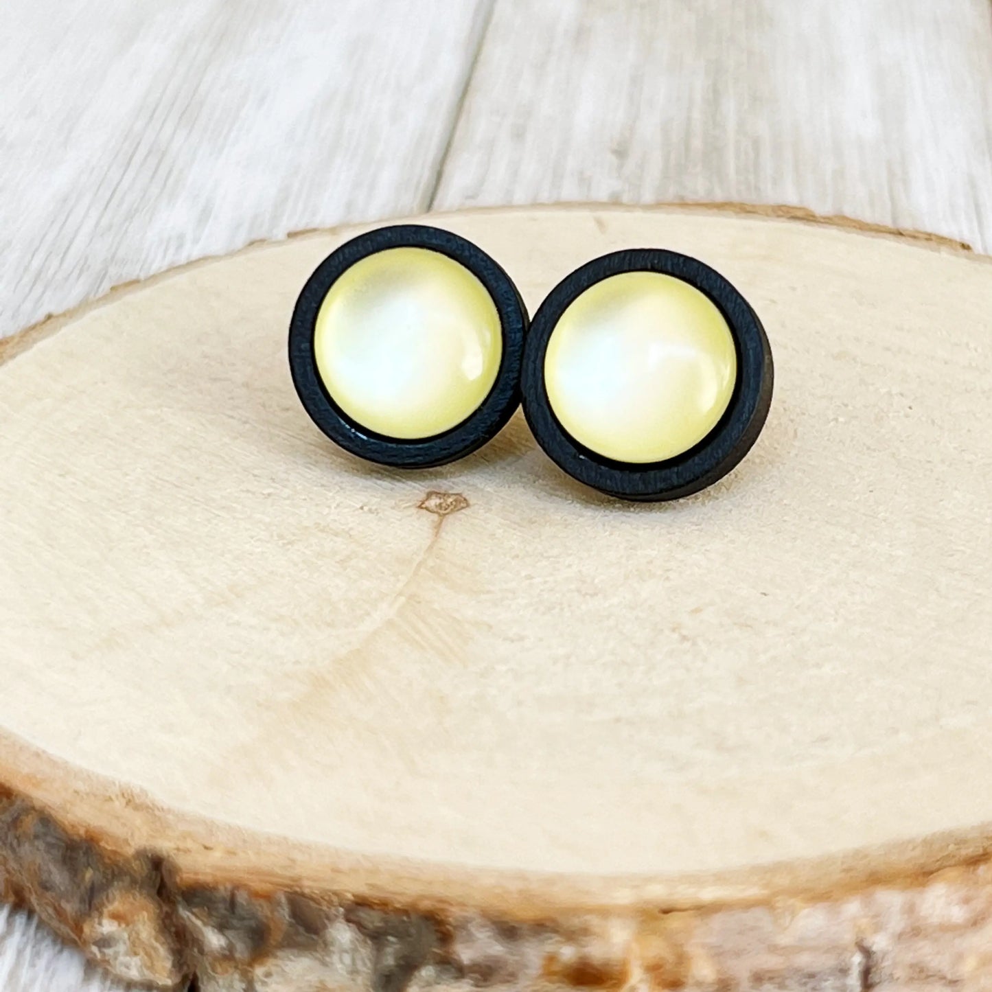 Pair of round earrings with yellow centers and black outer rims on a wooden surface.