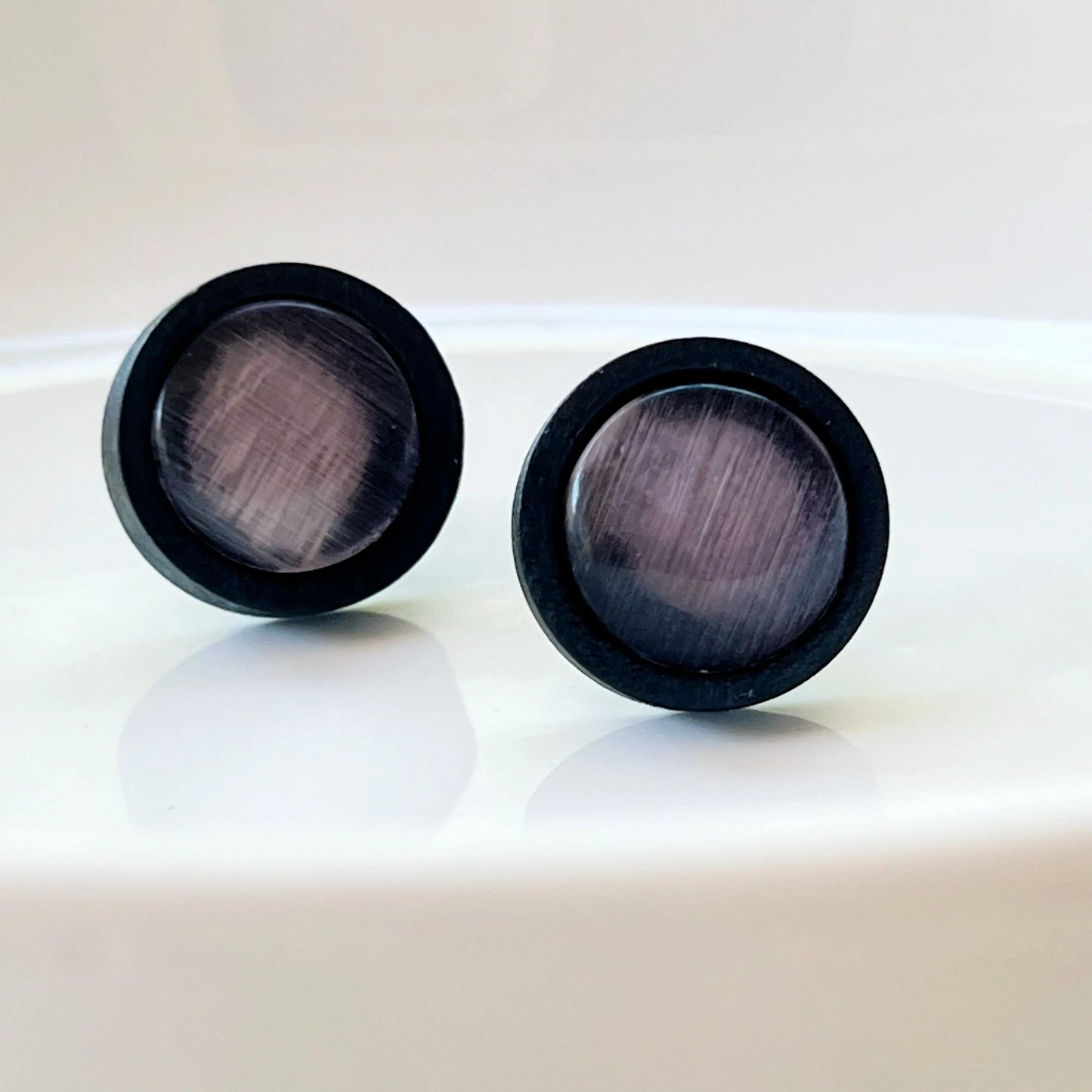 Pair of black earrings with reflective gray purple glass centers on a light background