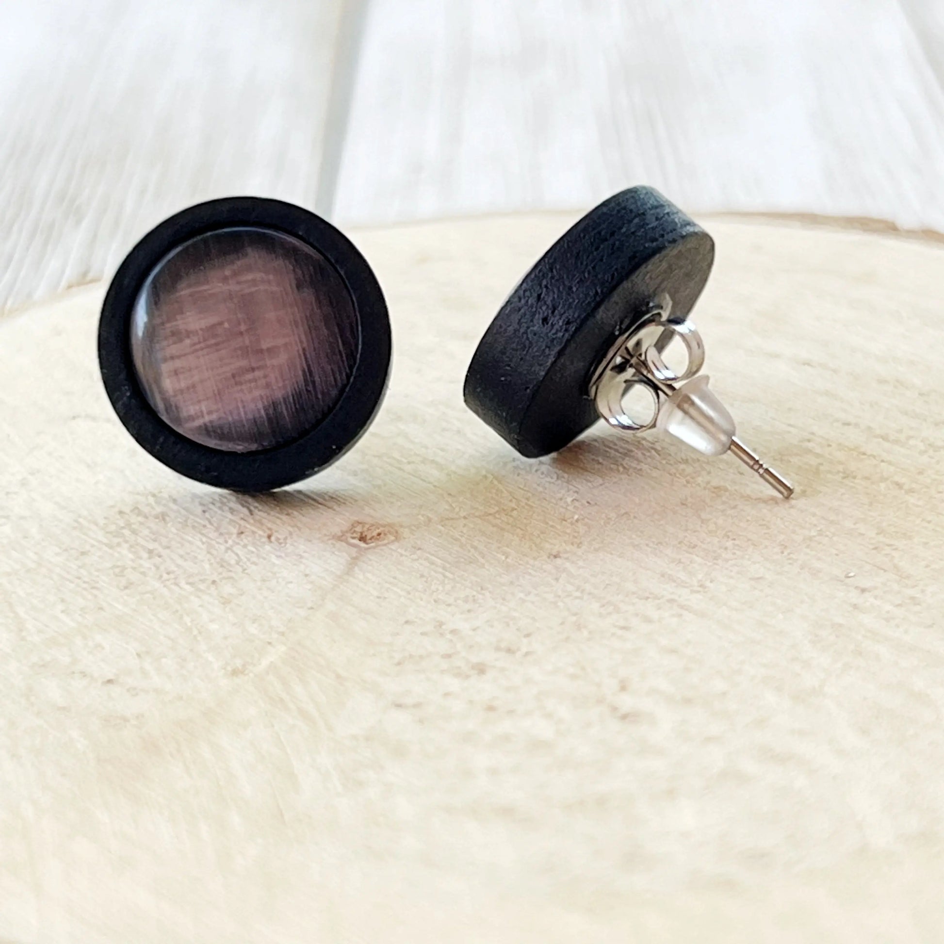 Black round earrings with mauve centers on a light wooden surface showing the back of the earrings 