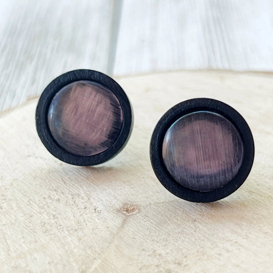 Round mauve gray glass stud earrings with black wood border displayed on light wood