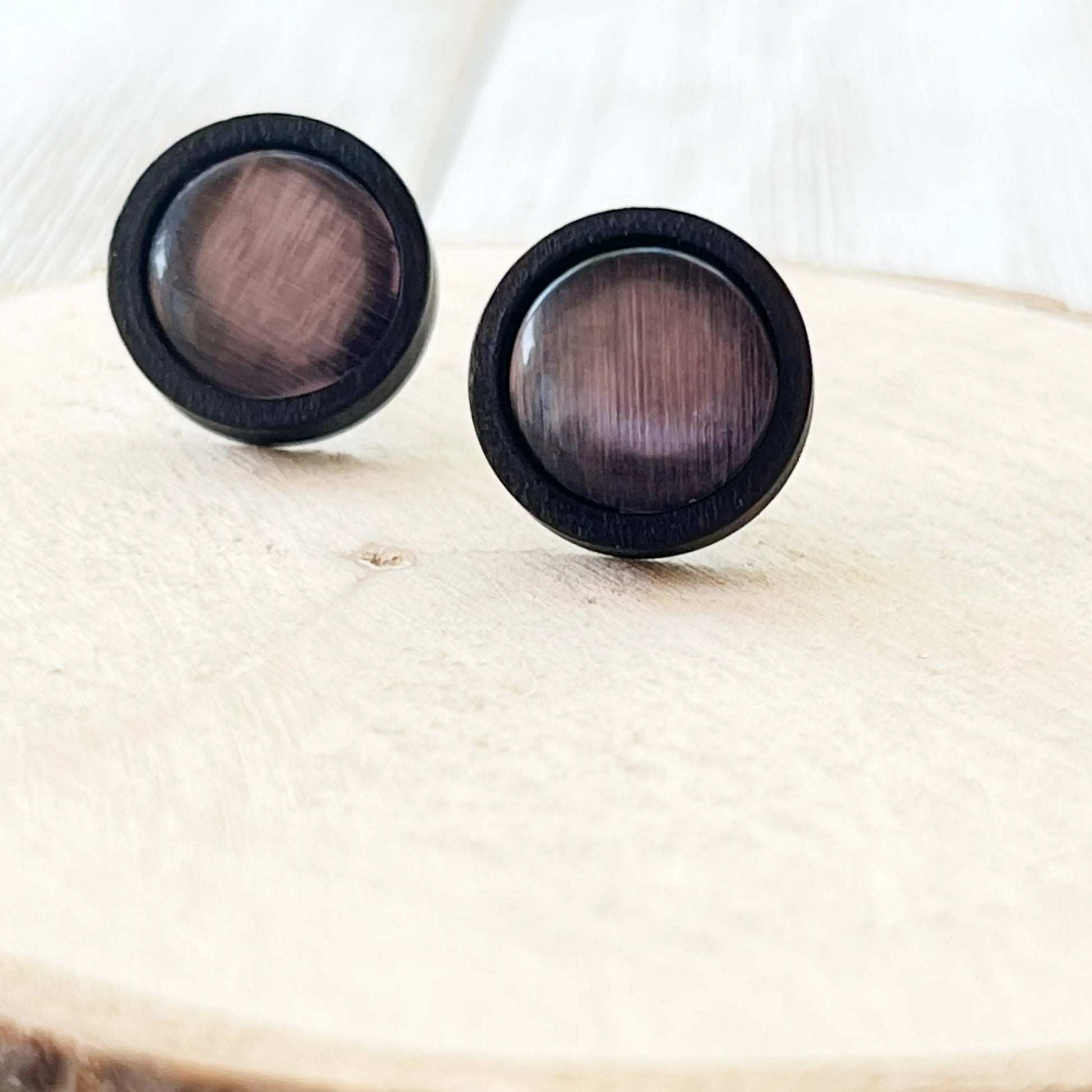 Pair of round earrings with a mauve center and black outer rim on a light wooden surface.
