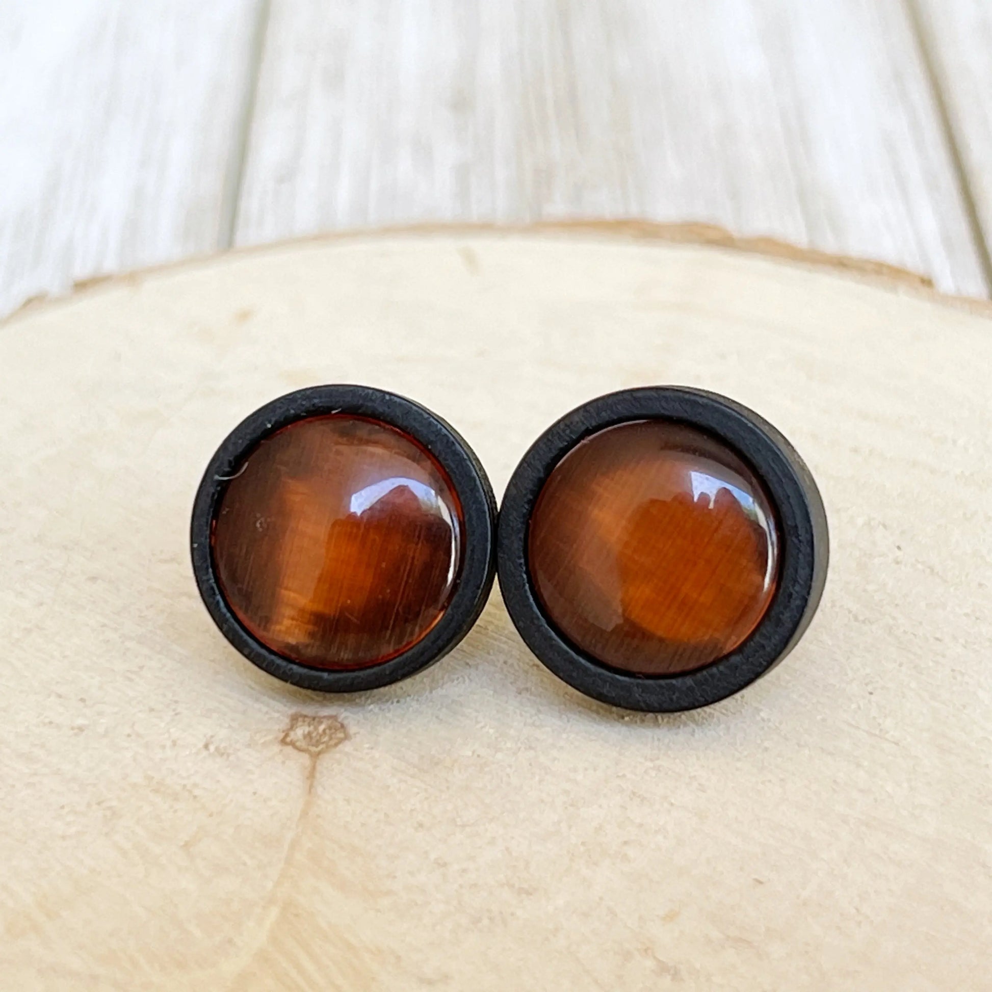 Round orange resin stud earrings with black wood borders displayed on a light wood surface