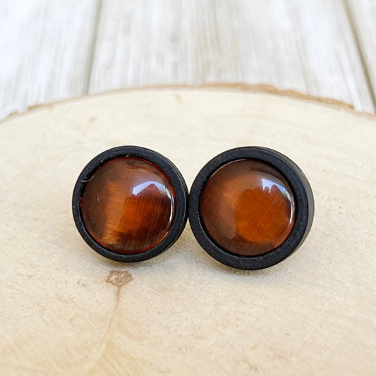 Round orange resin stud earrings with black wood borders displayed on a light wood surface