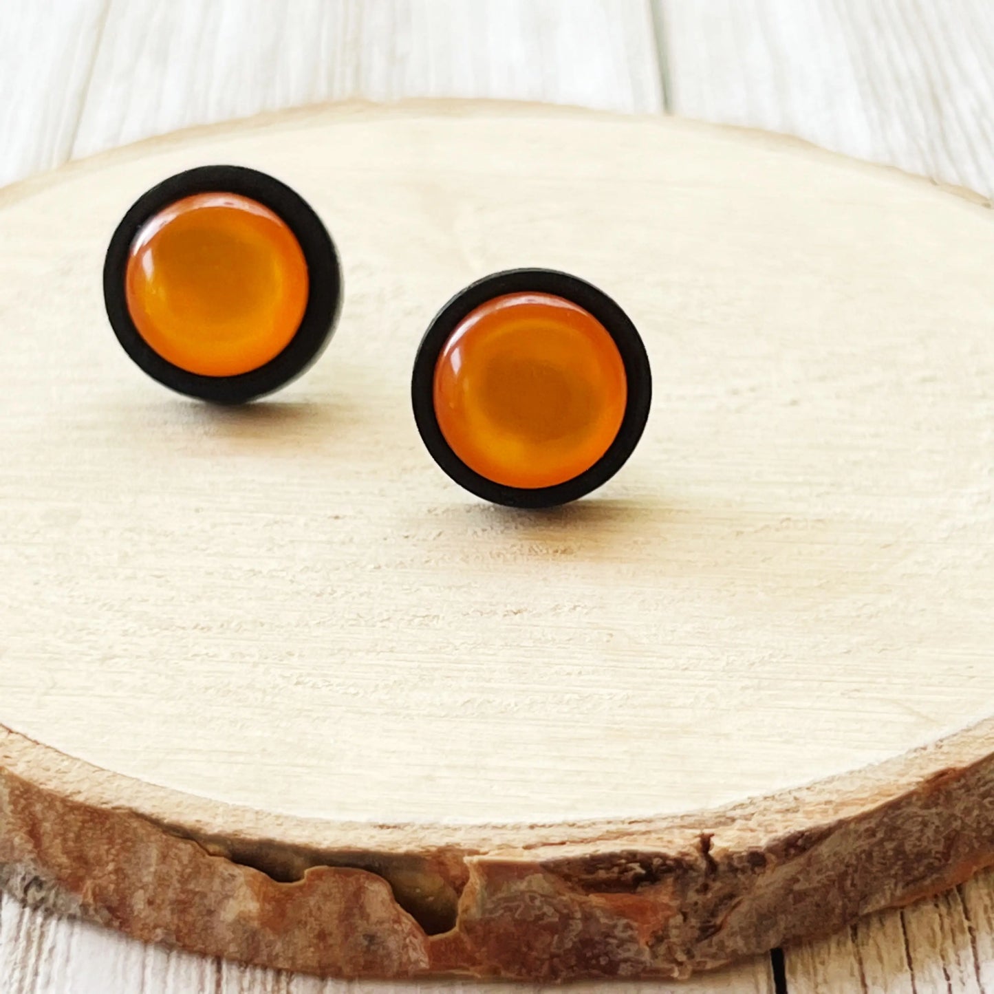 Pair of round orange earrings with black rims on a wood slice surface