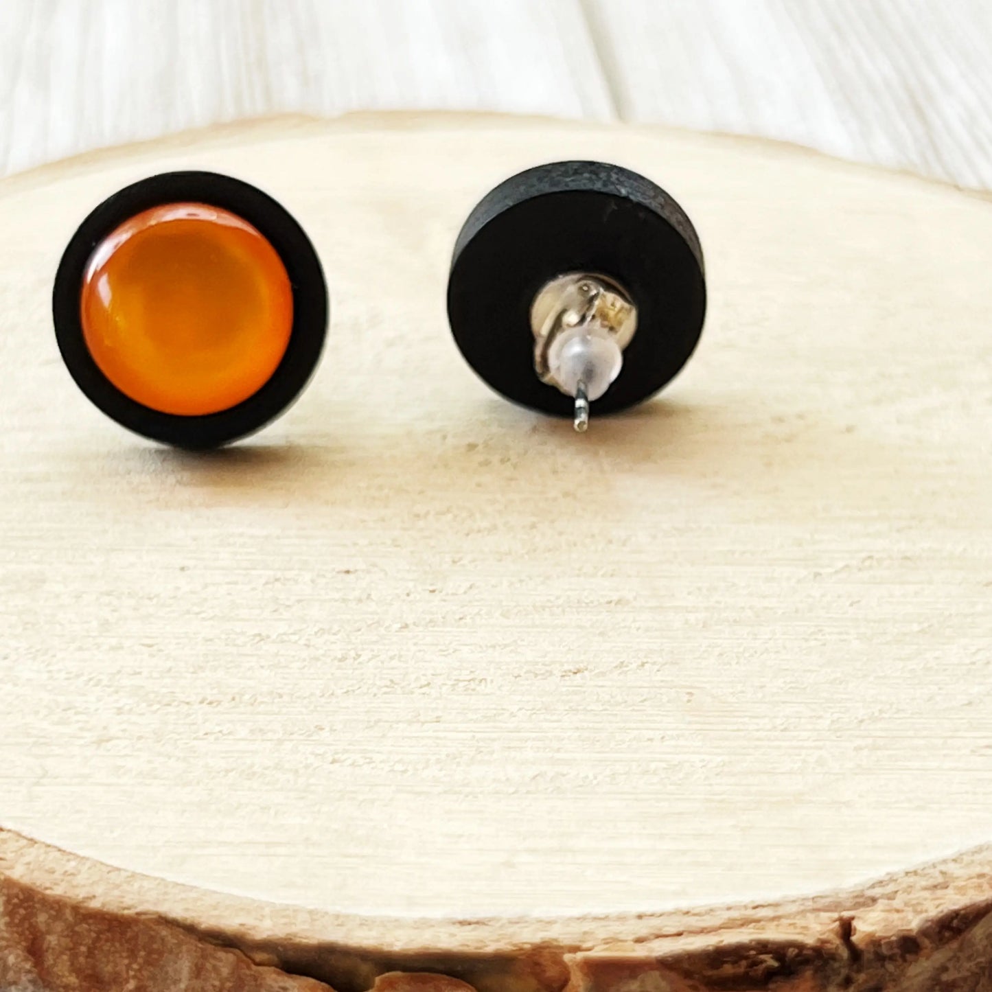 Back of a pair of earrings with black and orange circular designs on a wooden surface