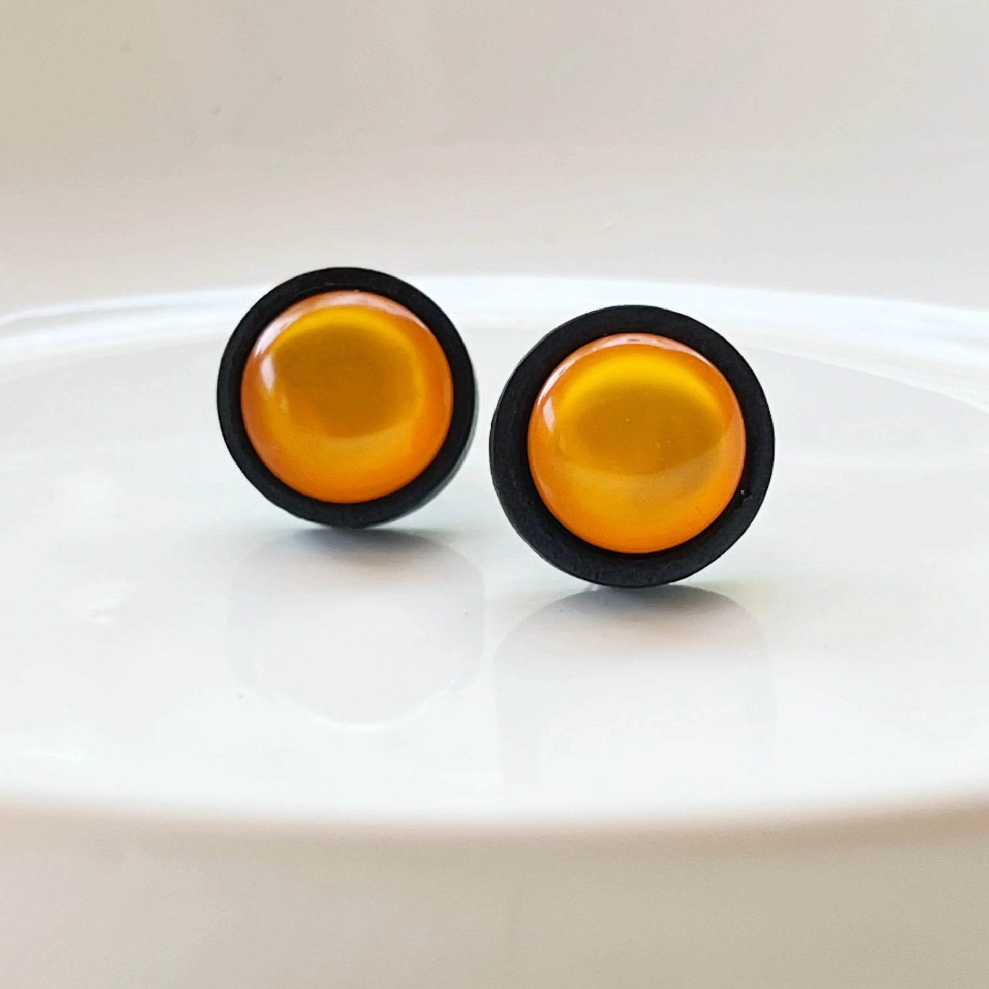 Round orange earrings with black rims on a white background