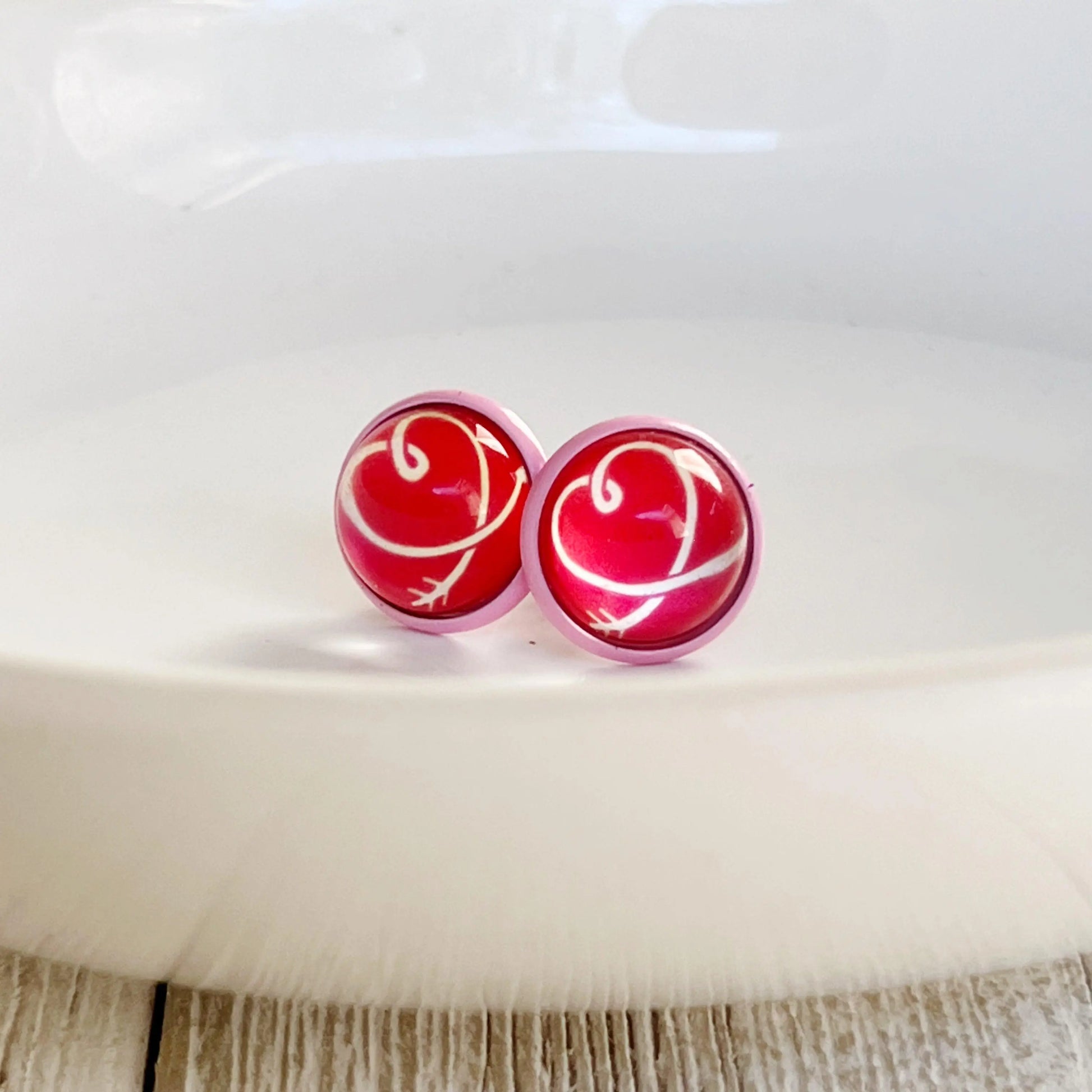 Pair of red earrings with a white design on a white surface.