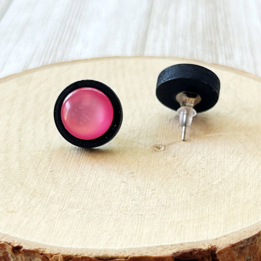 Back of black-framed earrings with pink centers on a wooden surface