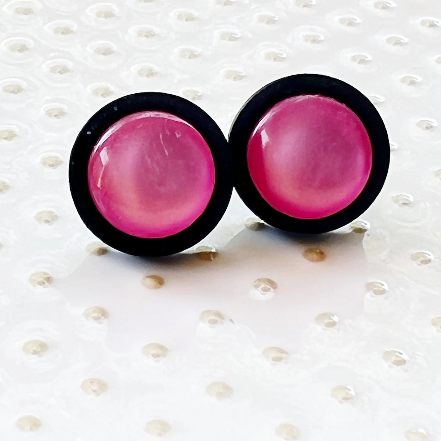 Pair of pink earrings with black rims on a cream glass background