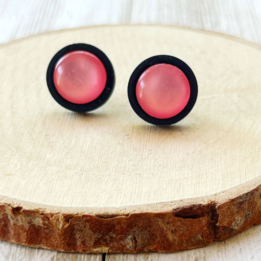 Round pink resin stud earrings with black wood border displayed on a wood slice