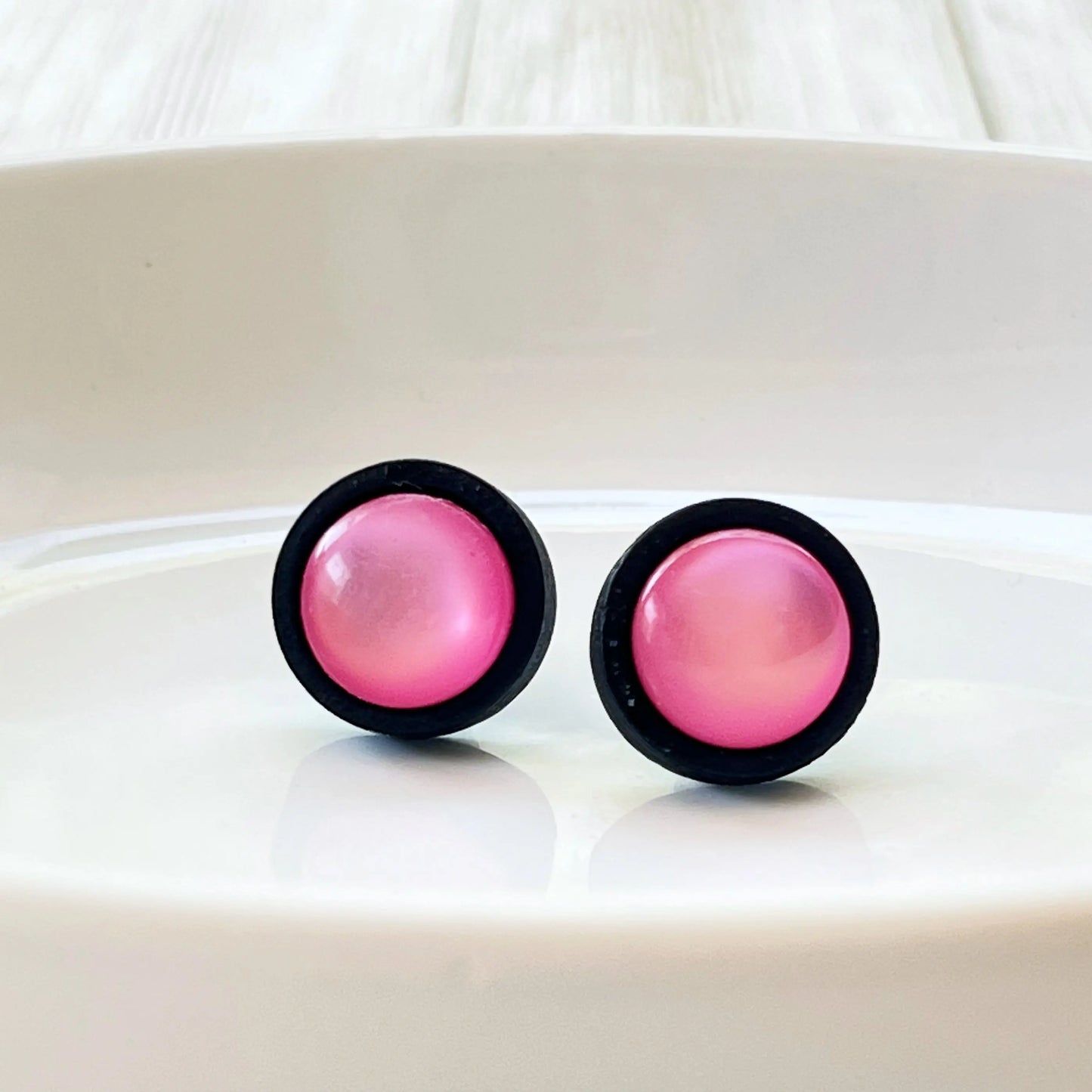Pair of pink earrings with black rims on a white glass surface