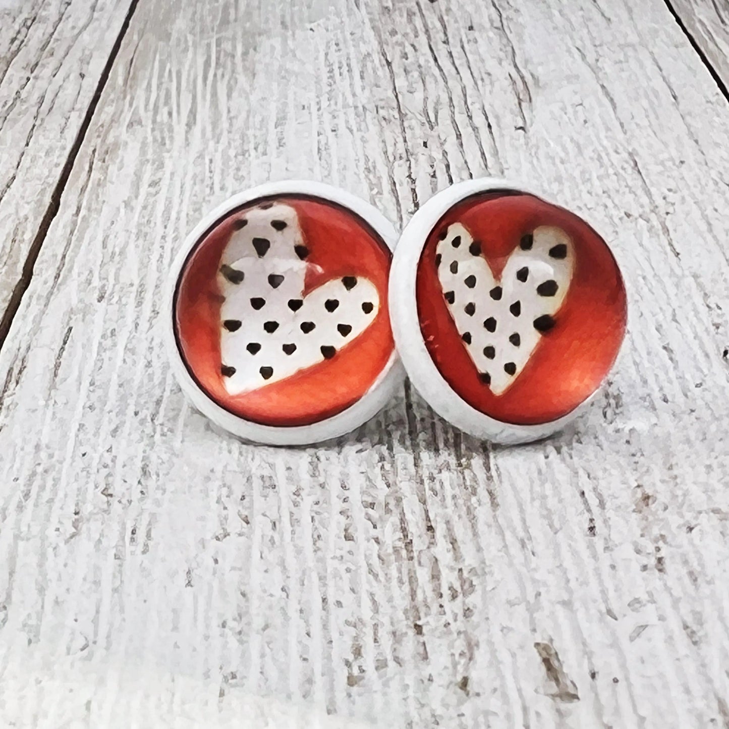 Heart-shaped earrings with red and white design on a whitewashed wooden surface
