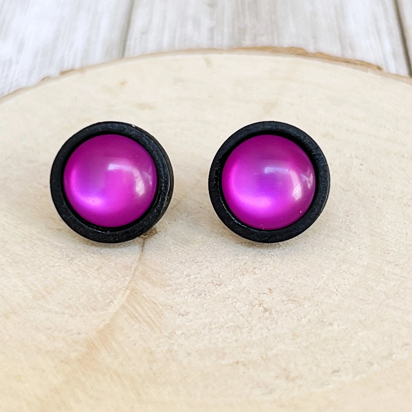 Pair of purple round earrings with black rims on a light wooden surface