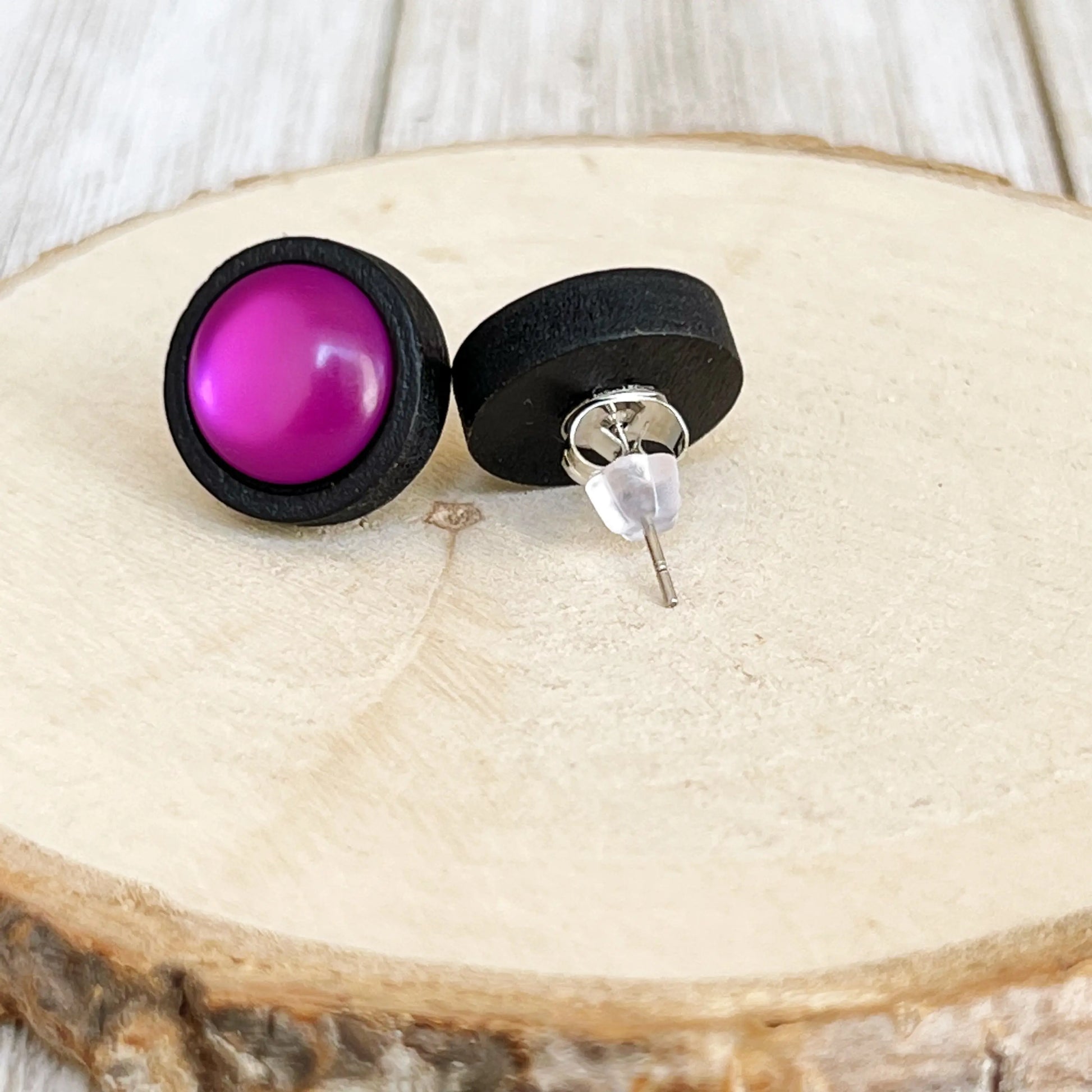 Back of a pair of earrings with purple and black round stones on a wooden surface
