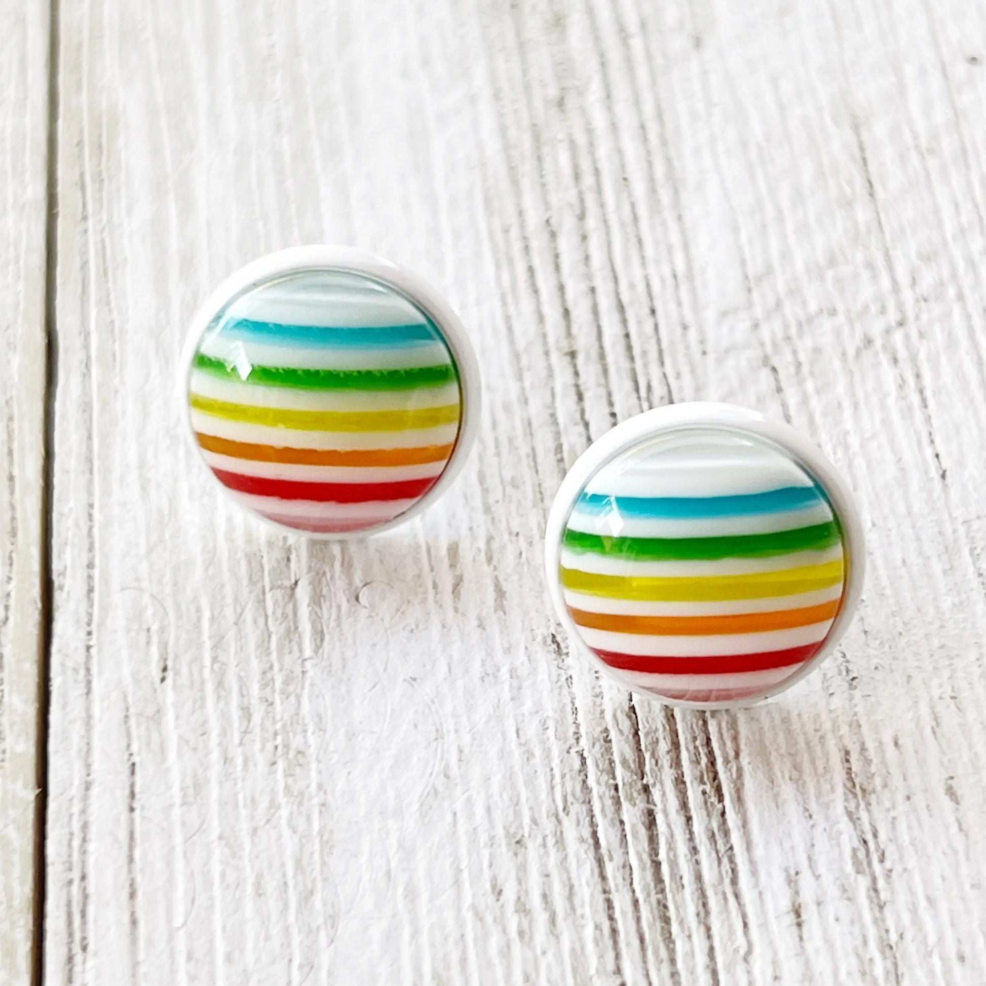 Pair of round earrings with colorful striped design on a wooden surface