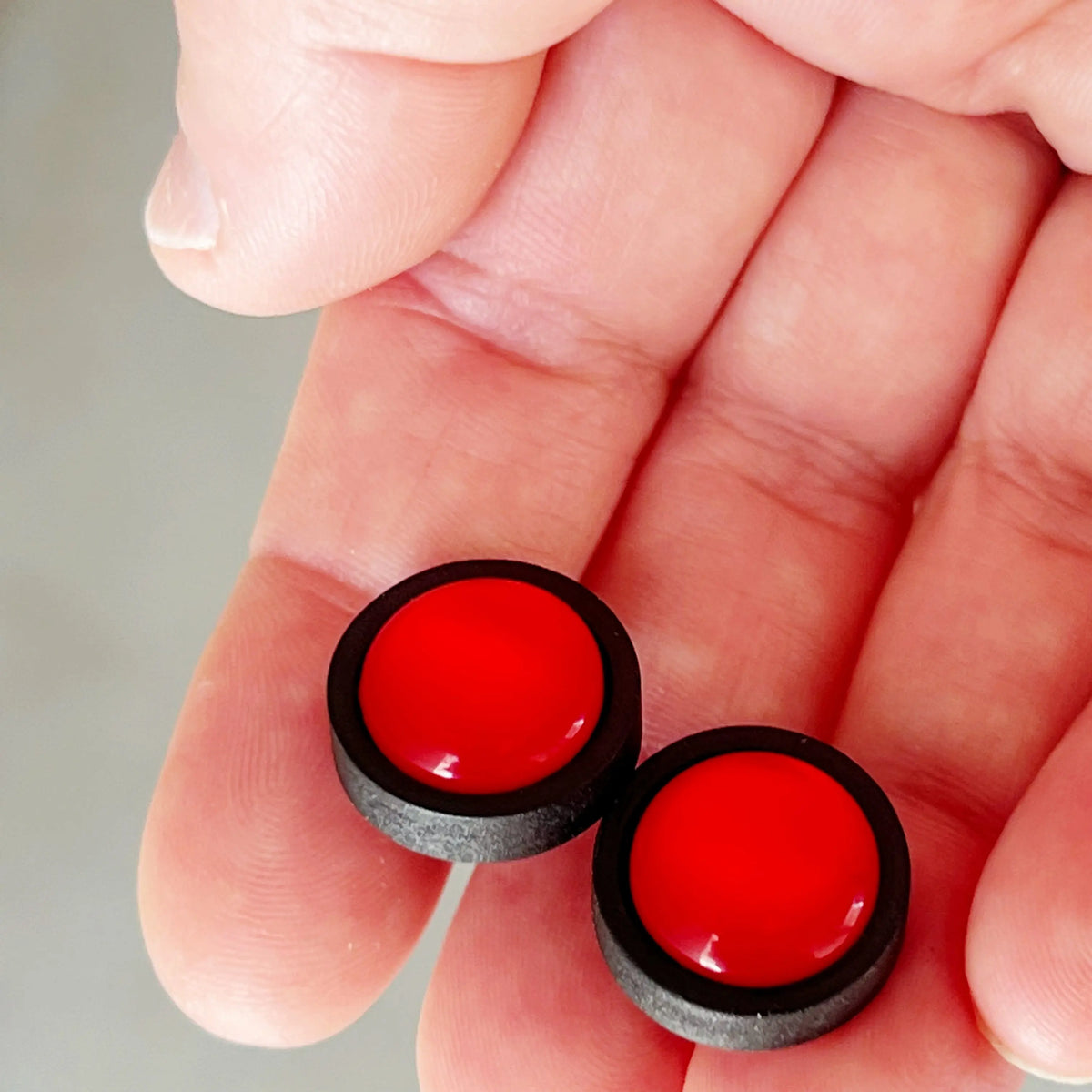 Red earrings with black borders held between fingers